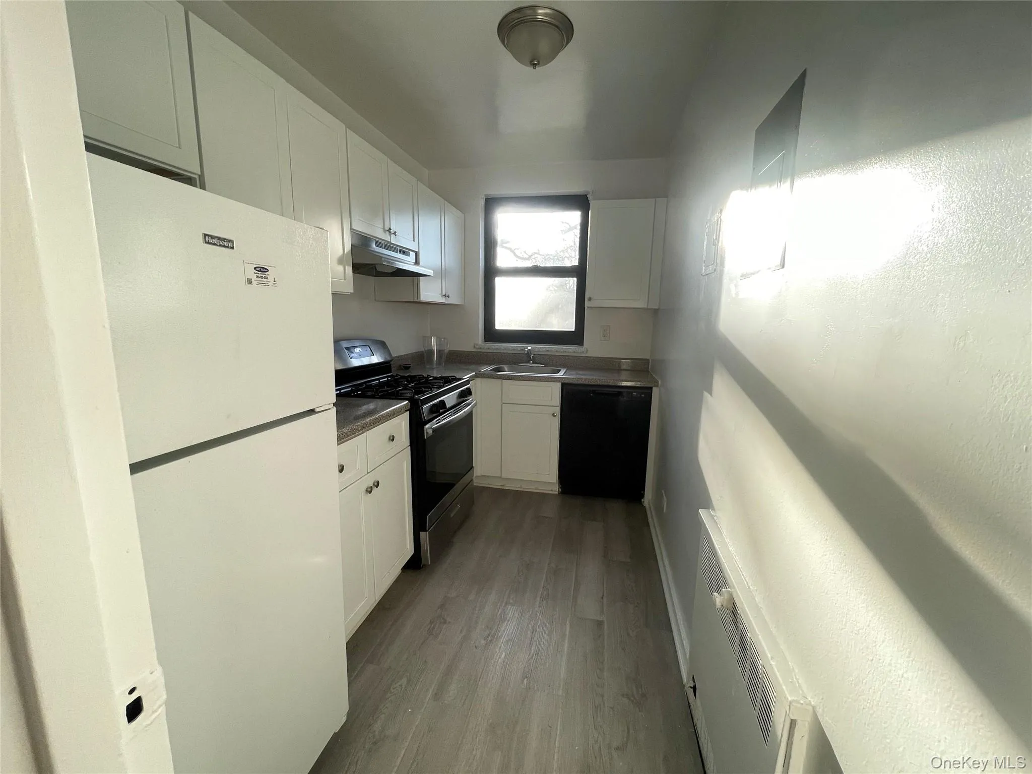 Kitchen featuring freestanding refrigerator, gas stove, white cabinetry, dishwasher, and dark wood-style floors Kitchen featuring freestanding refrigerator, gas stove, white cabinetry, dishwasher, and dark wood-style floors