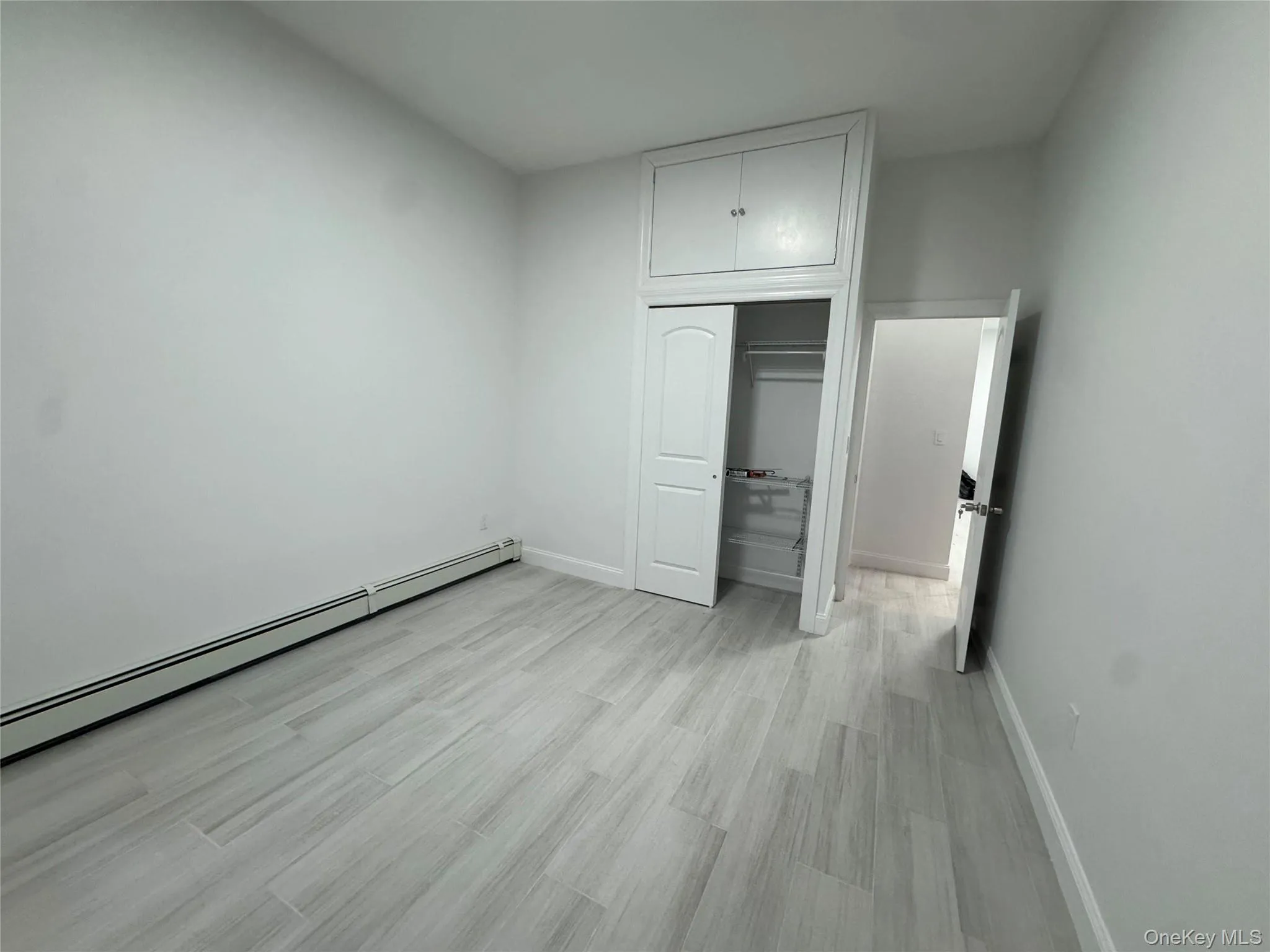 Unfurnished bedroom featuring a baseboard heating unit, light wood-style flooring, and a closet Unfurnished bedroom featuring a baseboard heating unit, light wood-style flooring, and a closet