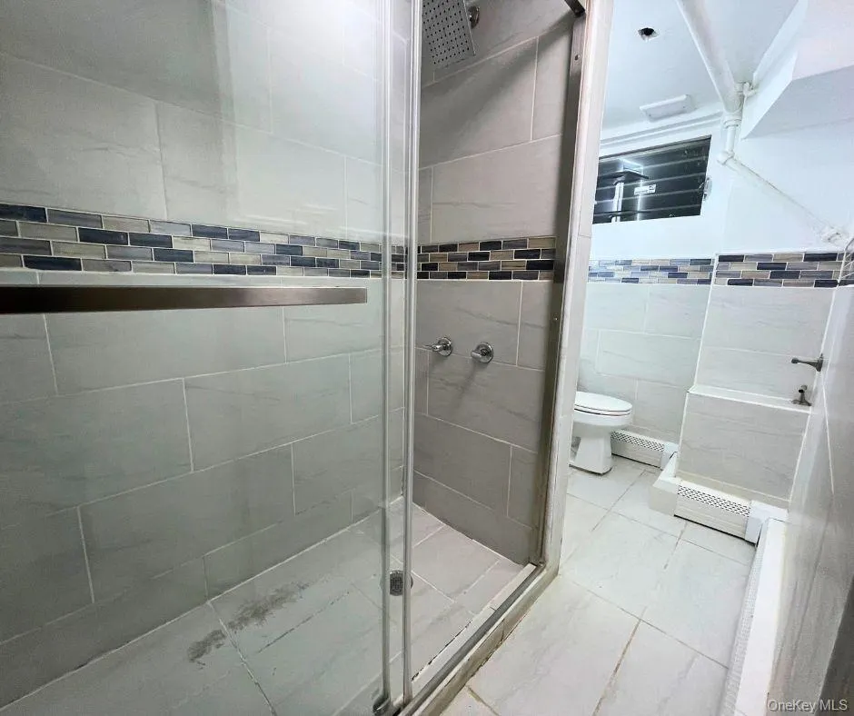 Bathroom featuring tile walls, a shower stall, and a baseboard radiator Bathroom featuring tile walls, a shower stall, and a baseboard radiator