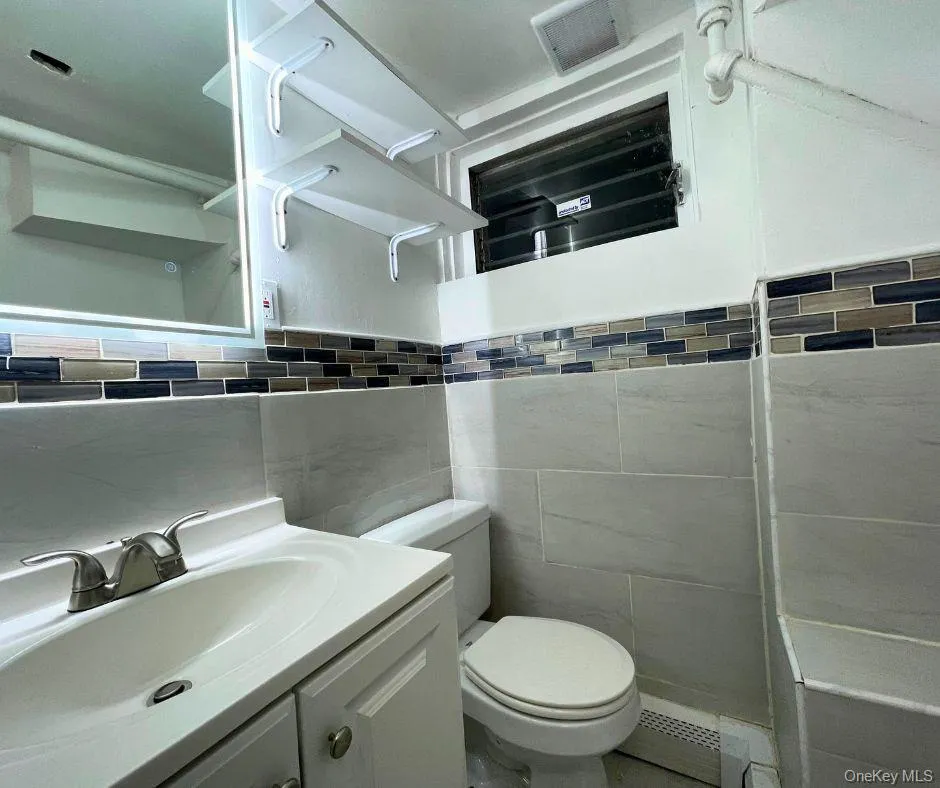 Half bath featuring tile walls, vanity, and a baseboard radiator Half bath featuring tile walls, vanity, and a baseboard radiator