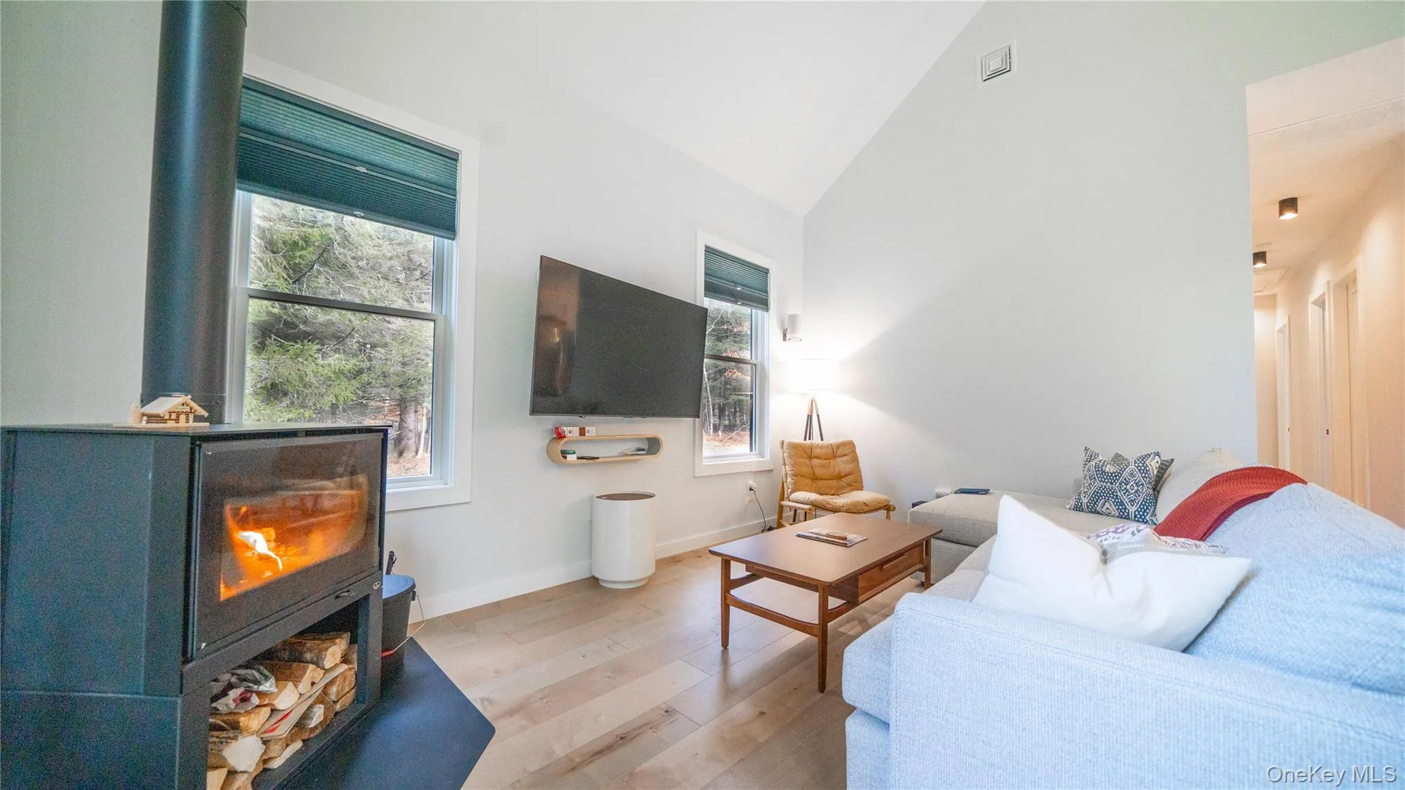 Living area with light wood-style floors, high vaulted ceiling, and a wood stove Living area with light wood-style floors, high vaulted ceiling, and a wood stove