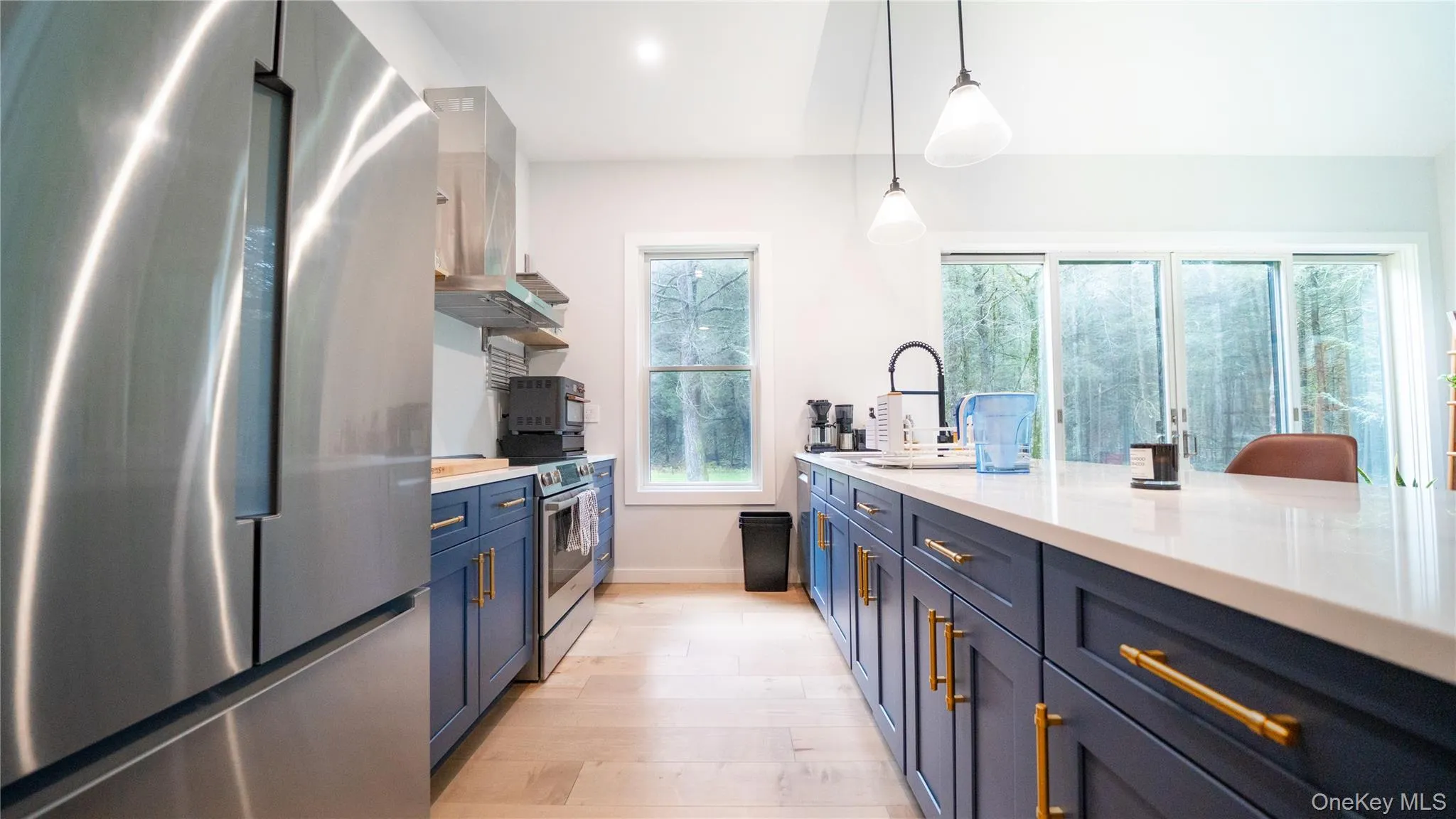 Kitchen featuring appliances with stainless steel finishes, blue cabinetry, decorative light fixtures, range hood, and light stone countertops Kitchen featuring appliances with stainless steel finishes, blue cabinetry, decorative light fixtures, range hood, and light stone countertops