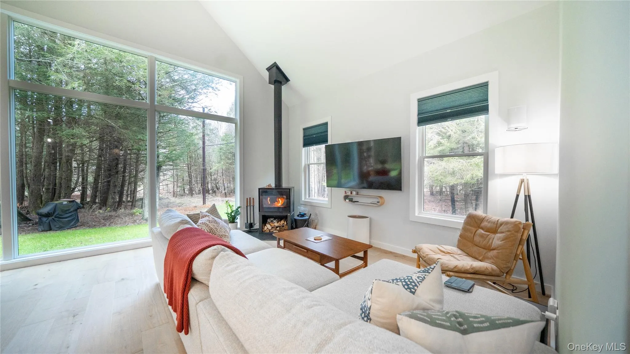 Living area featuring a wood stove, wood finished floors, and high vaulted ceiling Living area featuring a wood stove, wood finished floors, and high vaulted ceiling