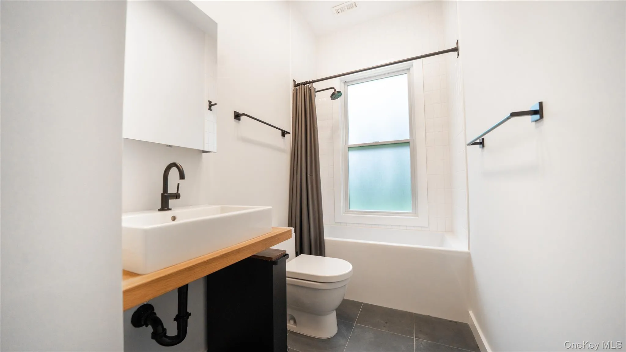 Full bathroom featuring shower / tub combo with curtain, vanity, and dark tile patterned flooring Full bathroom featuring shower / tub combo with curtain, vanity, and dark tile patterned flooring