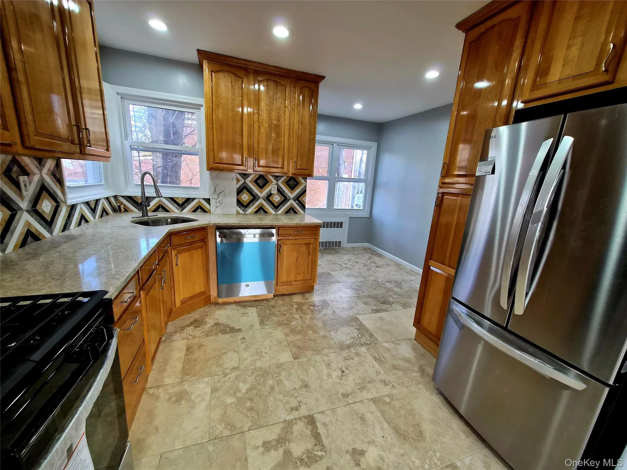 Kitchen featuring stainless steel appliances, brown cabinets, light stone counters, recessed lighting, and tasteful backsplash Kitchen featuring stainless steel appliances, brown cabinets, light stone counters, recessed lighting, and tasteful backsplash