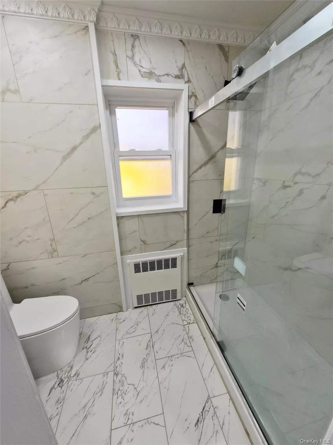 Full bath featuring light marble finish flooring, a marble finish shower, radiator, and tile walls Full bath featuring light marble finish flooring, a marble finish shower, radiator, and tile walls