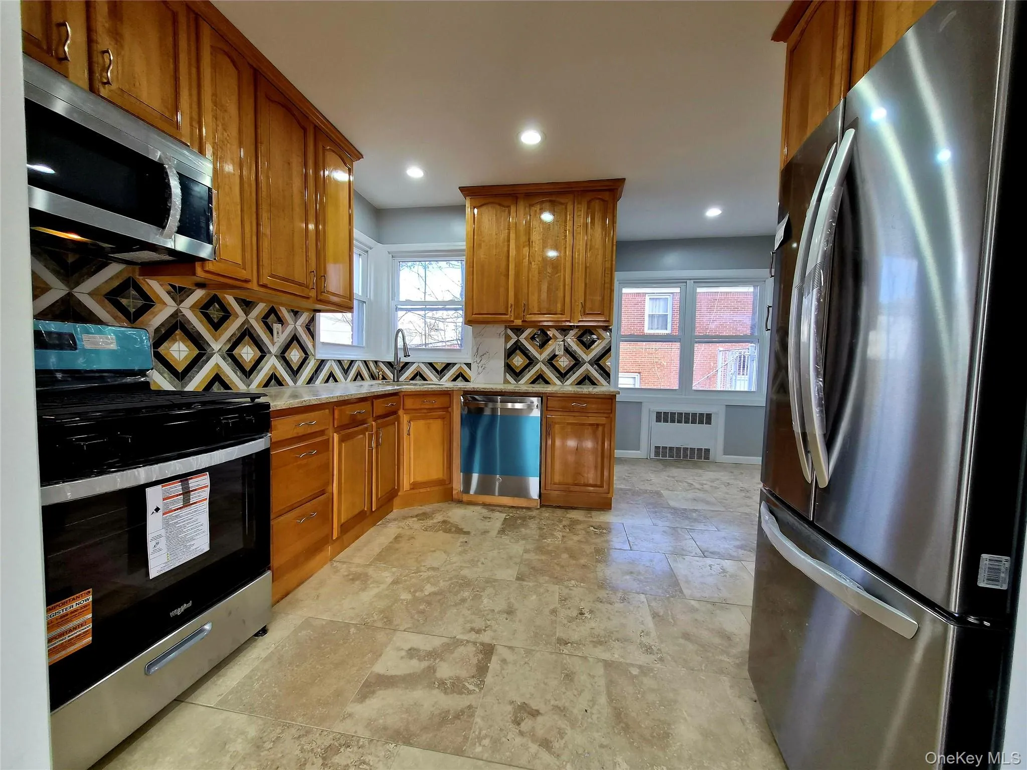 Kitchen featuring appliances with stainless steel finishes, brown cabinets, tasteful backsplash, recessed lighting, and stone tile floors Kitchen featuring appliances with stainless steel finishes, brown cabinets, tasteful backsplash, recessed lighting, and stone tile floors