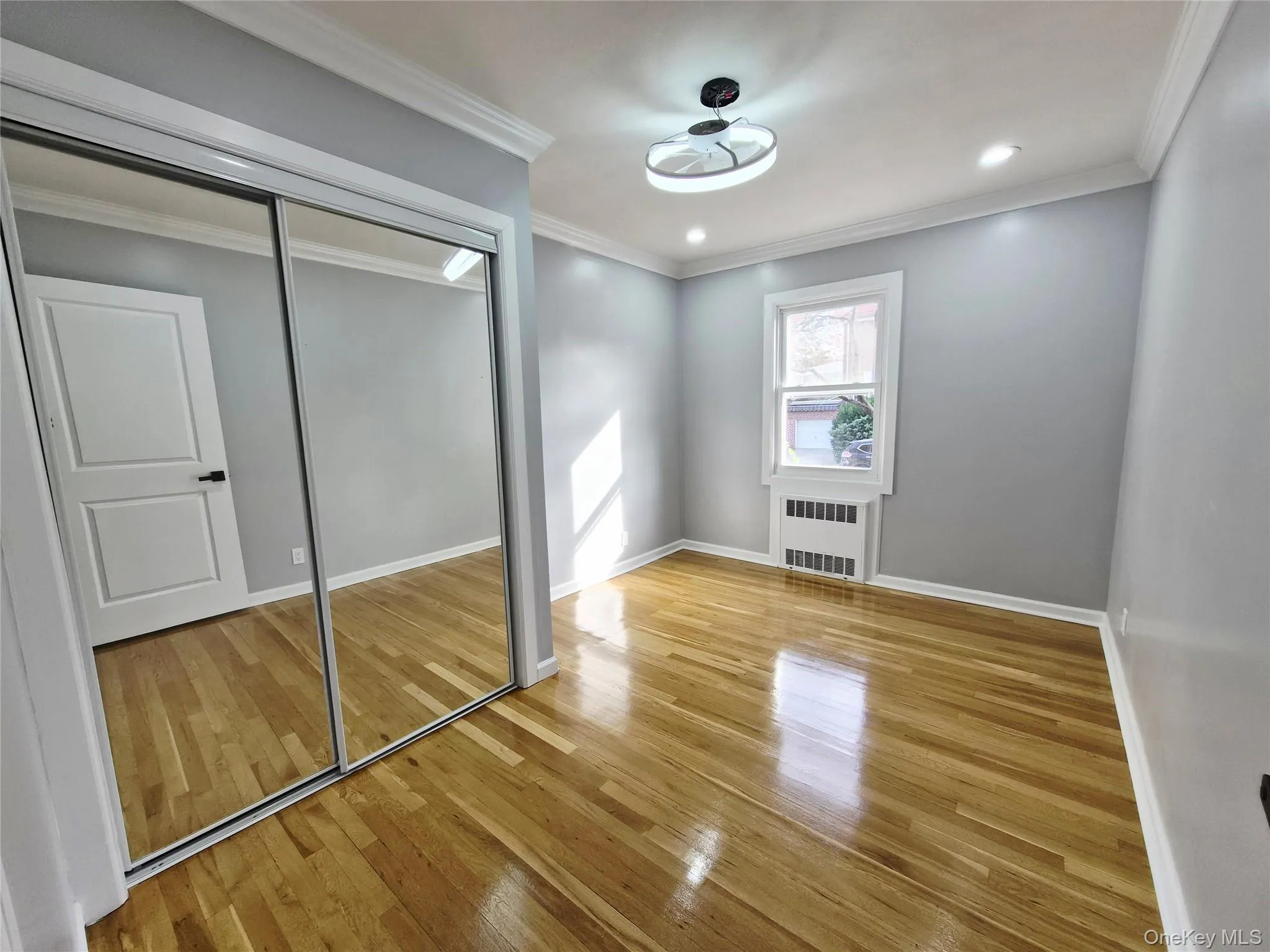 Unfurnished bedroom with light wood-style flooring, a closet, ornamental molding, radiator heating unit, and recessed lighting Unfurnished bedroom with light wood-style flooring, a closet, ornamental molding, radiator heating unit, and recessed lighting