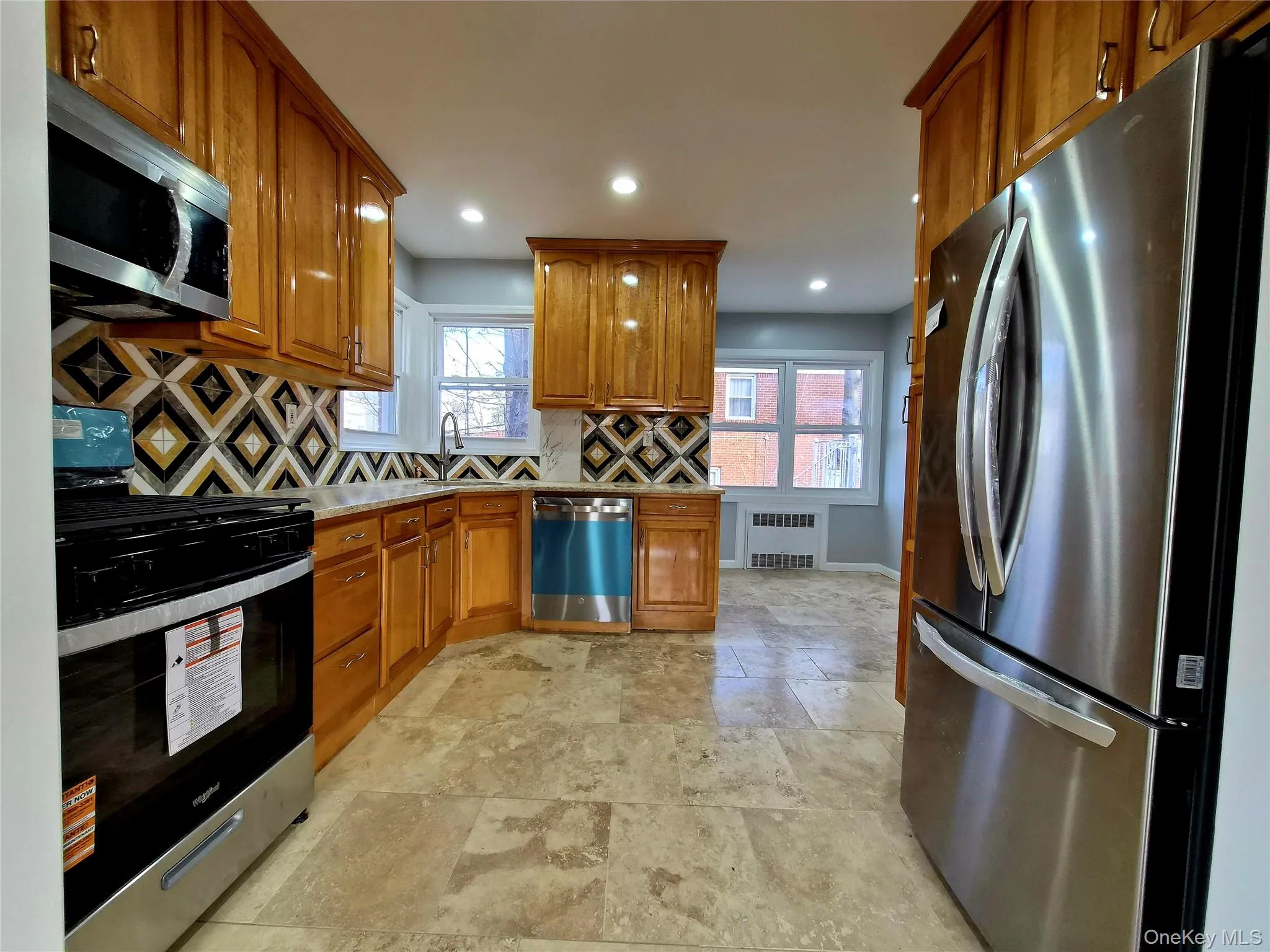Kitchen featuring appliances with stainless steel finishes, brown cabinets, decorative backsplash, radiator heating unit, and recessed lighting Kitchen featuring appliances with stainless steel finishes, brown cabinets, decorative backsplash, radiator heating unit, and recessed lighting