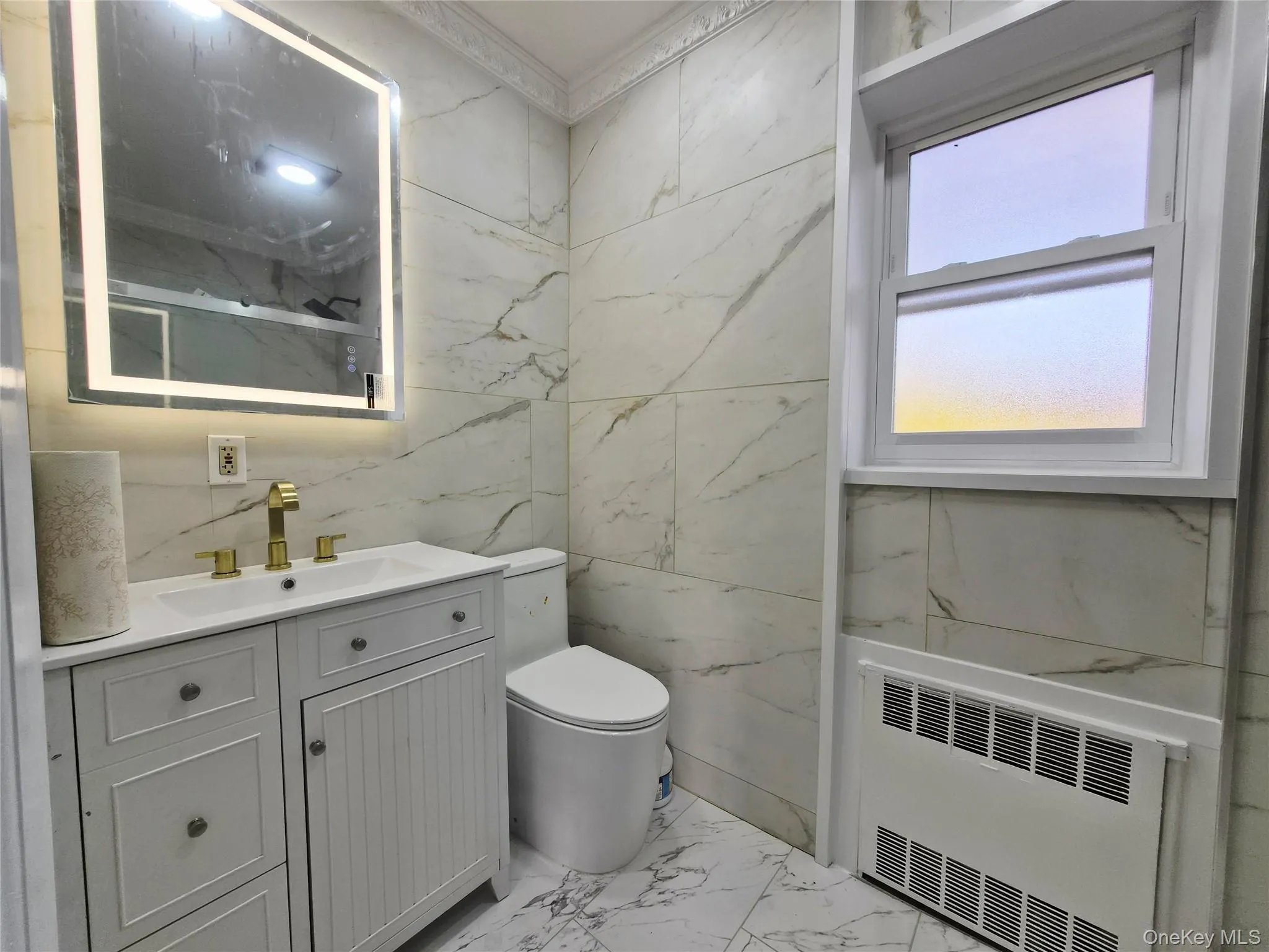 Full bath with tile walls, light marble finish floors, vanity, radiator heating unit, and a marble finish shower Full bath with tile walls, light marble finish floors, vanity, radiator heating unit, and a marble finish shower