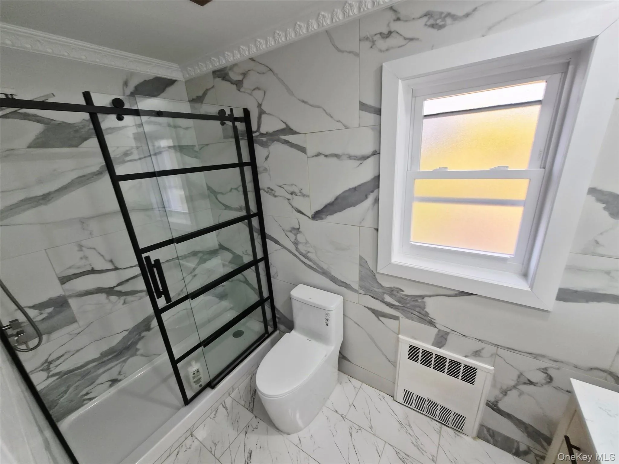 Bathroom with light marble finish floors, a marble finish shower, ornamental molding, tile walls, and radiator Bathroom with light marble finish floors, a marble finish shower, ornamental molding, tile walls, and radiator