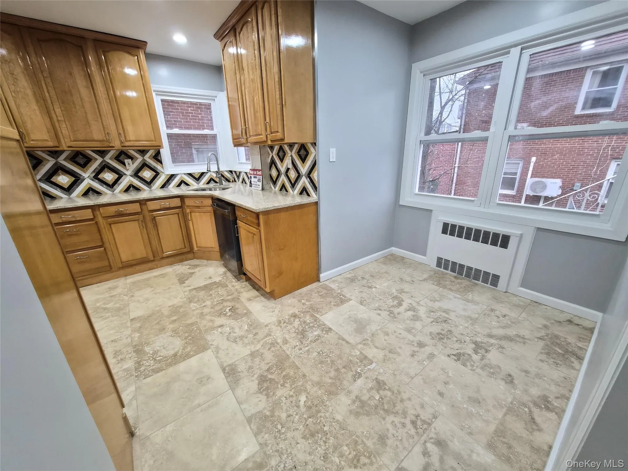Kitchen featuring brown cabinets, decorative backsplash, light stone counters, radiator, and recessed lighting Kitchen featuring brown cabinets, decorative backsplash, light stone counters, radiator, and recessed lighting