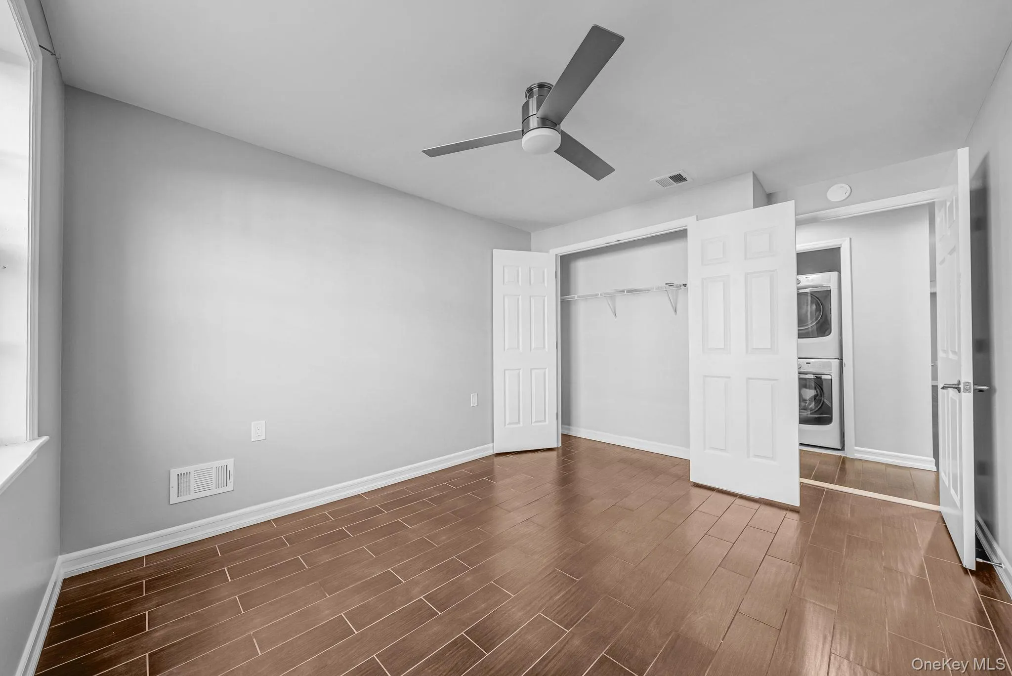 Unfurnished bedroom featuring a closet, wood finish floors, stacked washer / dryer, and ceiling fan Unfurnished bedroom featuring a closet, wood finish floors, stacked washer / dryer, and ceiling fan