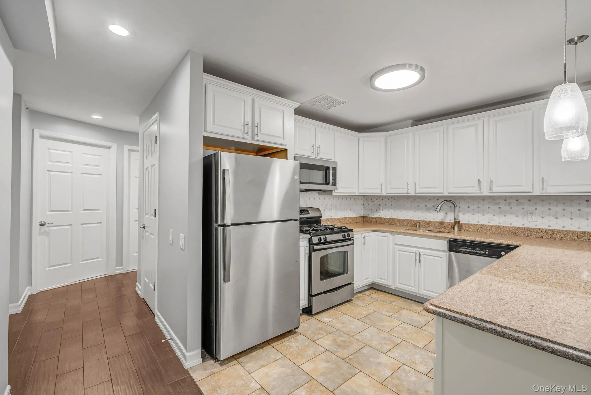 Kitchen with appliances with stainless steel finishes, pendant lighting, white cabinets, light stone countertops, and backsplash Kitchen with appliances with stainless steel finishes, pendant lighting, white cabinets, light stone countertops, and backsplash