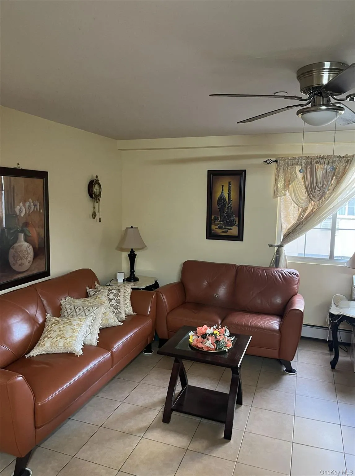 Living room featuring tile patterned flooring, a ceiling fan, and a baseboard heating unit Living room featuring tile patterned flooring, a ceiling fan, and a baseboard heating unit
