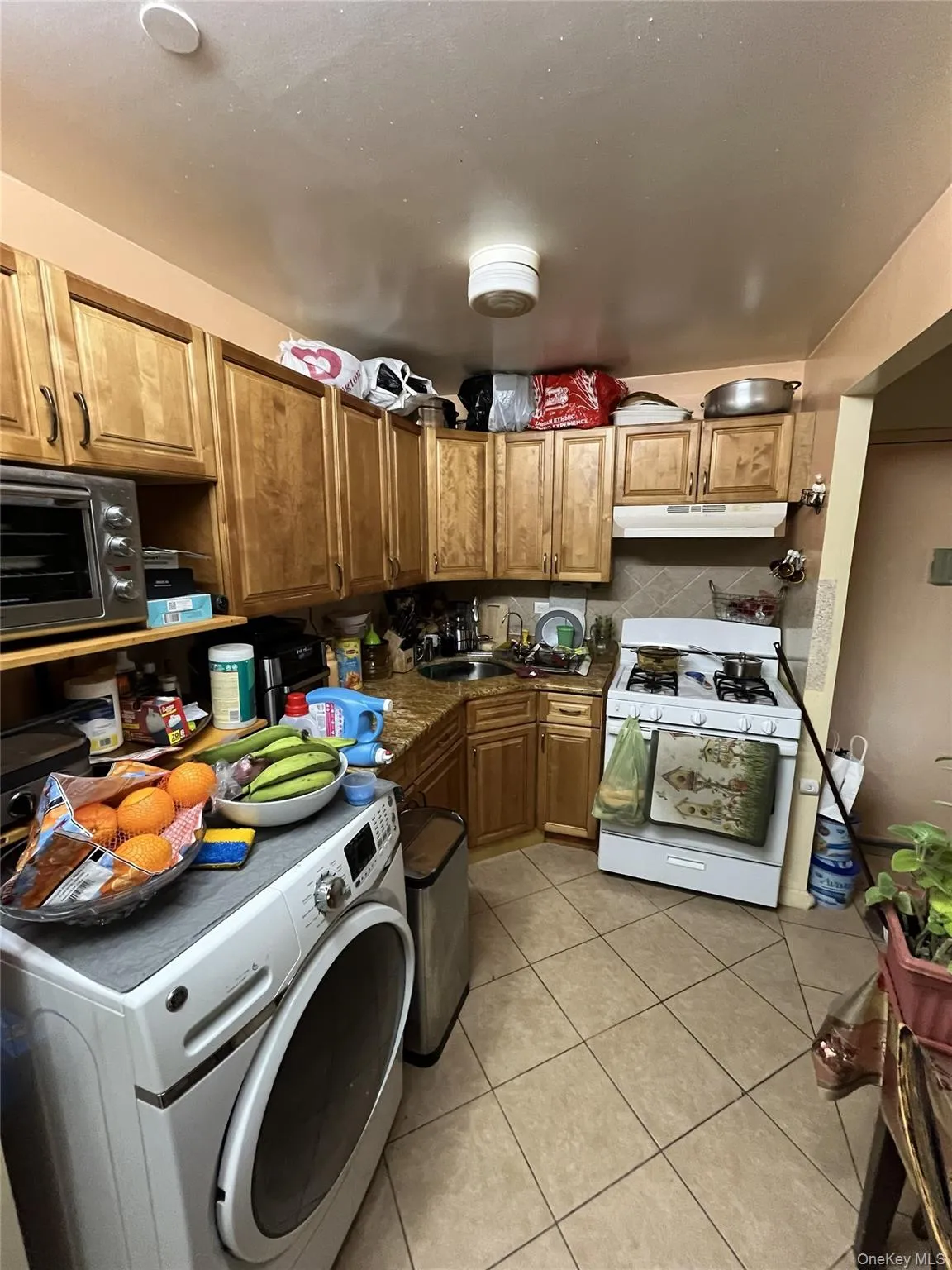 Kitchen featuring white gas stove, washer / clothes dryer, light tile patterned flooring, dark countertops, and under cabinet range hood Kitchen featuring white gas stove, washer / clothes dryer, light tile patterned flooring, dark countertops, and under cabinet range hood