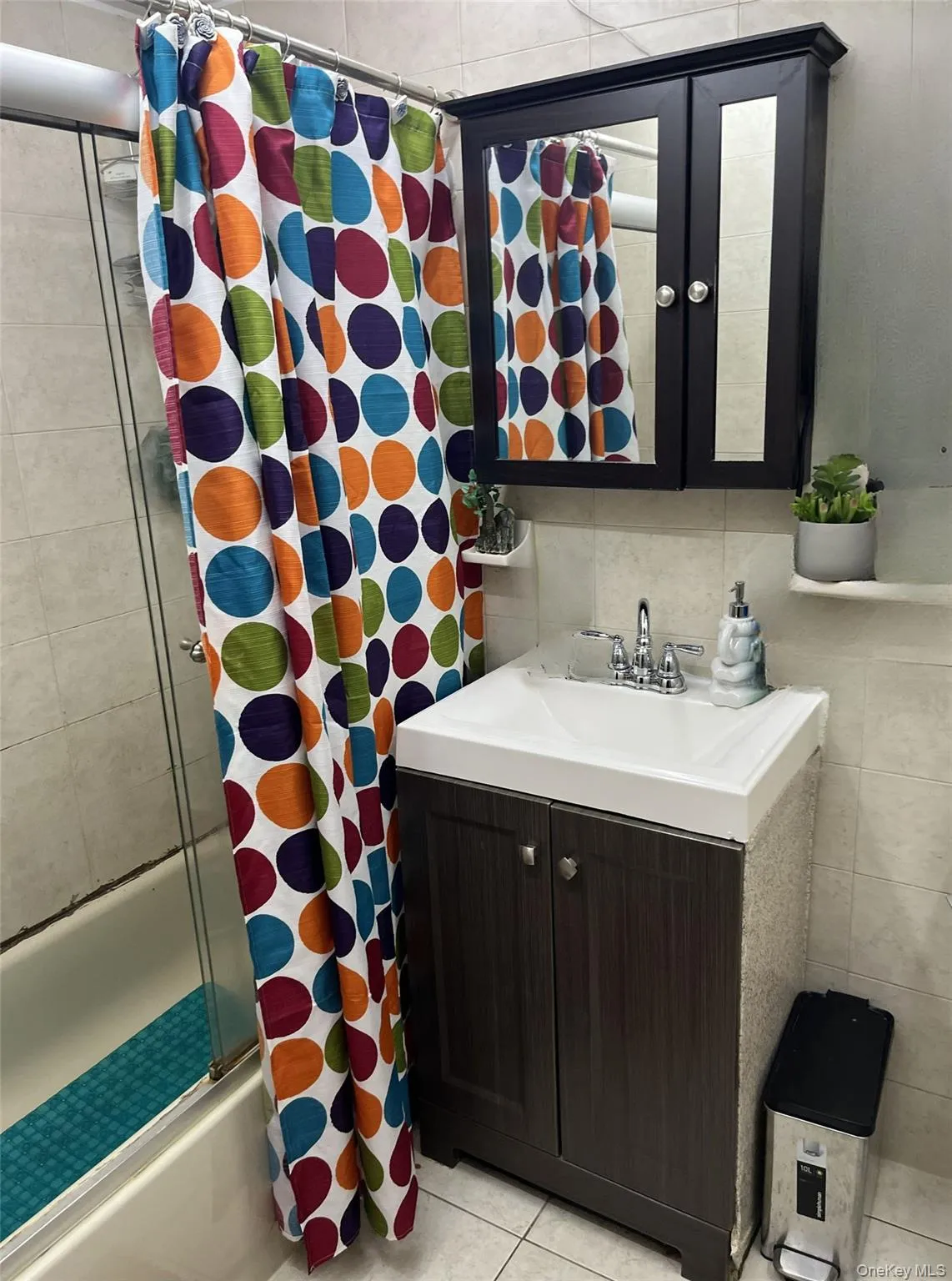 Full bathroom with tile walls, vanity, combined bath / shower with glass door, and light tile patterned floors Full bathroom with tile walls, vanity, combined bath / shower with glass door, and light tile patterned floors