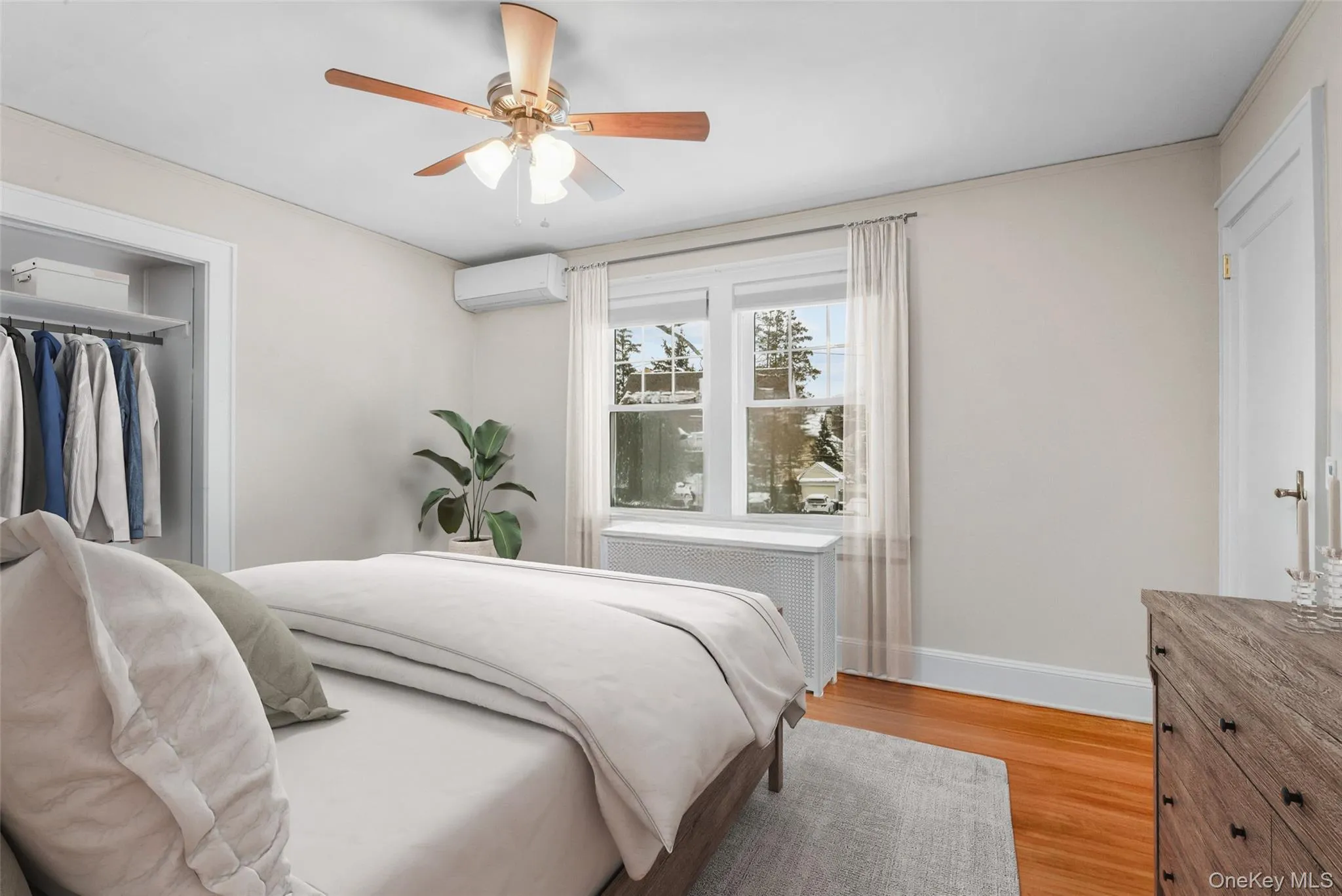 Bedroom with radiator, light wood finished floors, a wall mounted air conditioner, ceiling fan, and a closet Bedroom with radiator, light wood finished floors, a wall mounted air conditioner, ceiling fan, and a closet