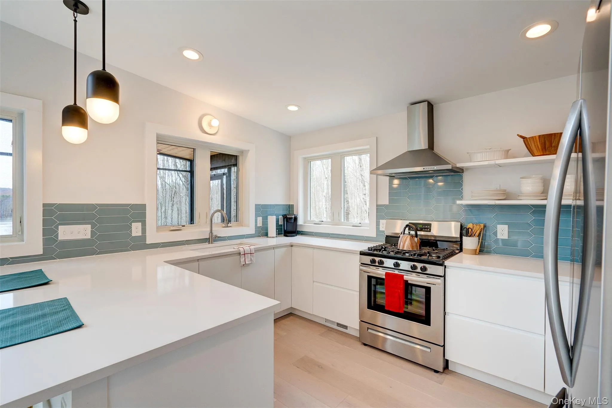 Kitchen with stainless steel appliances, wall chimney exhaust hood, decorative light fixtures, white cabinets, and decorative backsplash Kitchen with stainless steel appliances, wall chimney exhaust hood, decorative light fixtures, white cabinets, and decorative backsplash