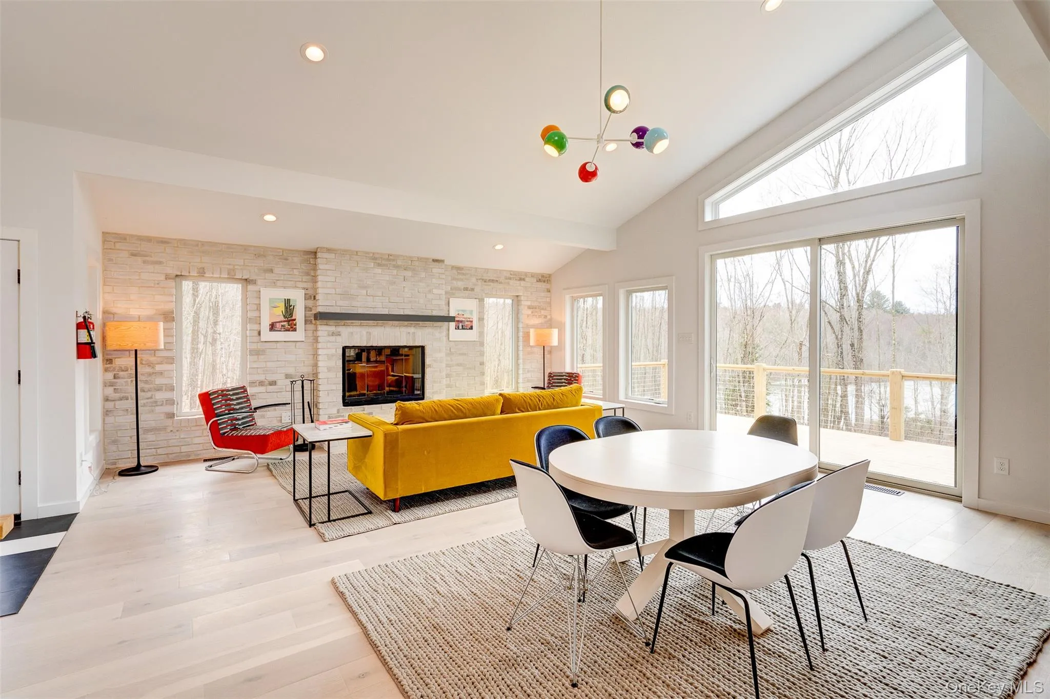 Dining space with healthy amount of natural light, light wood finished floors, a large fireplace, brick wall, and high vaulted ceiling Dining space with healthy amount of natural light, light wood finished floors, a large fireplace, brick wall, and high vaulted ceiling