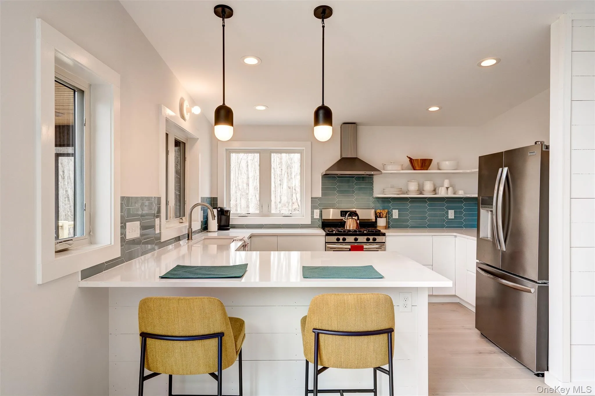 Kitchen featuring appliances with stainless steel finishes, a peninsula, a breakfast bar area, wall chimney range hood, and white cabinetry Kitchen featuring appliances with stainless steel finishes, a peninsula, a breakfast bar area, wall chimney range hood, and white cabinetry