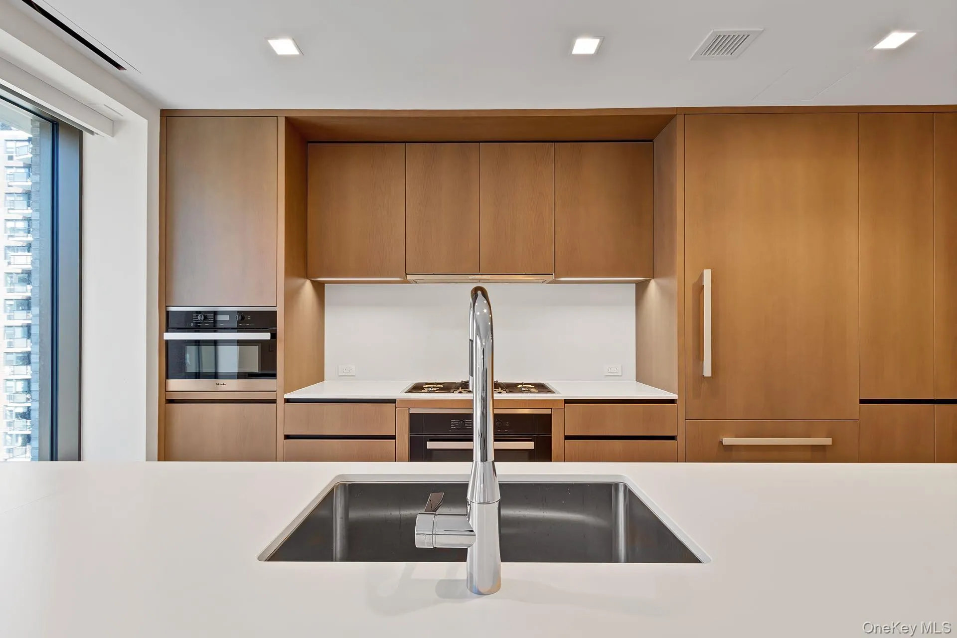 Kitchen featuring modern cabinets, stainless steel oven, light stone counters, and brown cabinetry Kitchen featuring modern cabinets, stainless steel oven, light stone counters, and brown cabinetry