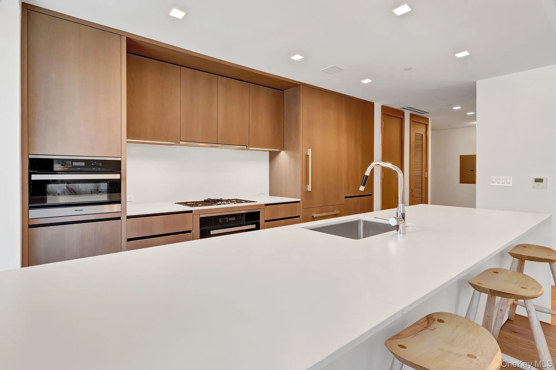 Kitchen with modern cabinets, recessed lighting, a breakfast bar, stainless steel oven, and light stone counters Kitchen with modern cabinets, recessed lighting, a breakfast bar, stainless steel oven, and light stone counters