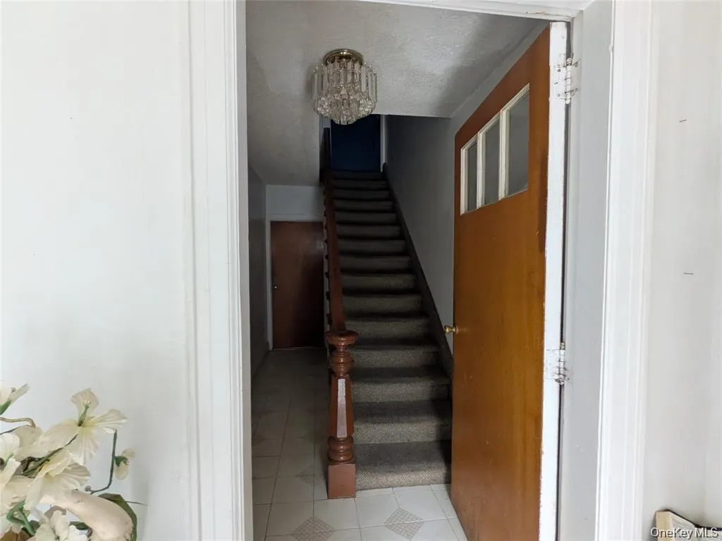 Stairway featuring a chandelier, tile patterned flooring, and a textured ceiling Stairway featuring a chandelier, tile patterned flooring, and a textured ceiling