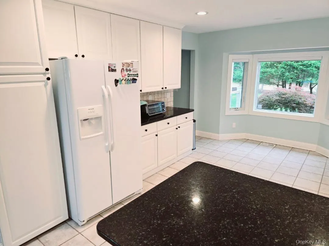 Kitchen featuring white refrigerator with ice dispenser, light tile patterned floors, white cabinetry, tasteful backsplash, and recessed lighting Kitchen featuring white refrigerator with ice dispenser, light tile patterned floors, white cabinetry, tasteful backsplash, and recessed lighting
