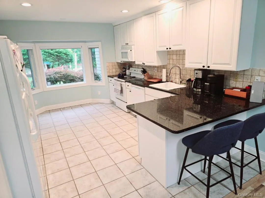 Kitchen with white appliances, white cabinetry, a kitchen bar, dark stone countertops, and a peninsula Kitchen with white appliances, white cabinetry, a kitchen bar, dark stone countertops, and a peninsula