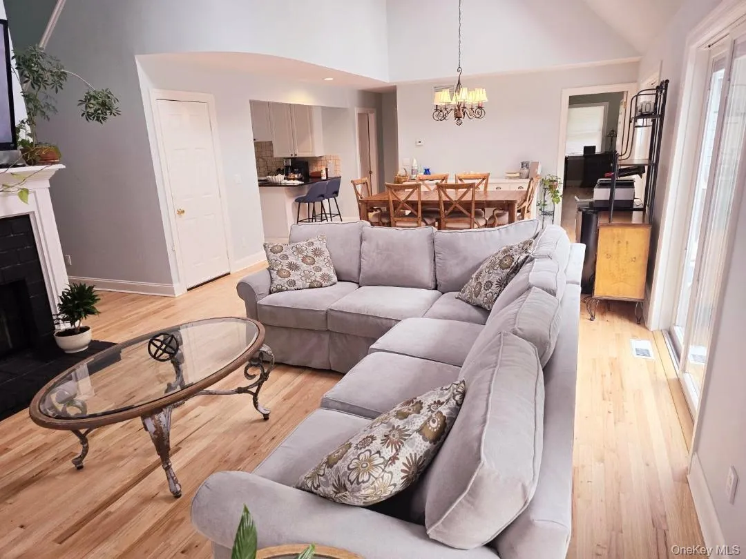 Living room featuring a fireplace with raised hearth, light wood finished floors, a chandelier, and high vaulted ceiling Living room featuring a fireplace with raised hearth, light wood finished floors, a chandelier, and high vaulted ceiling