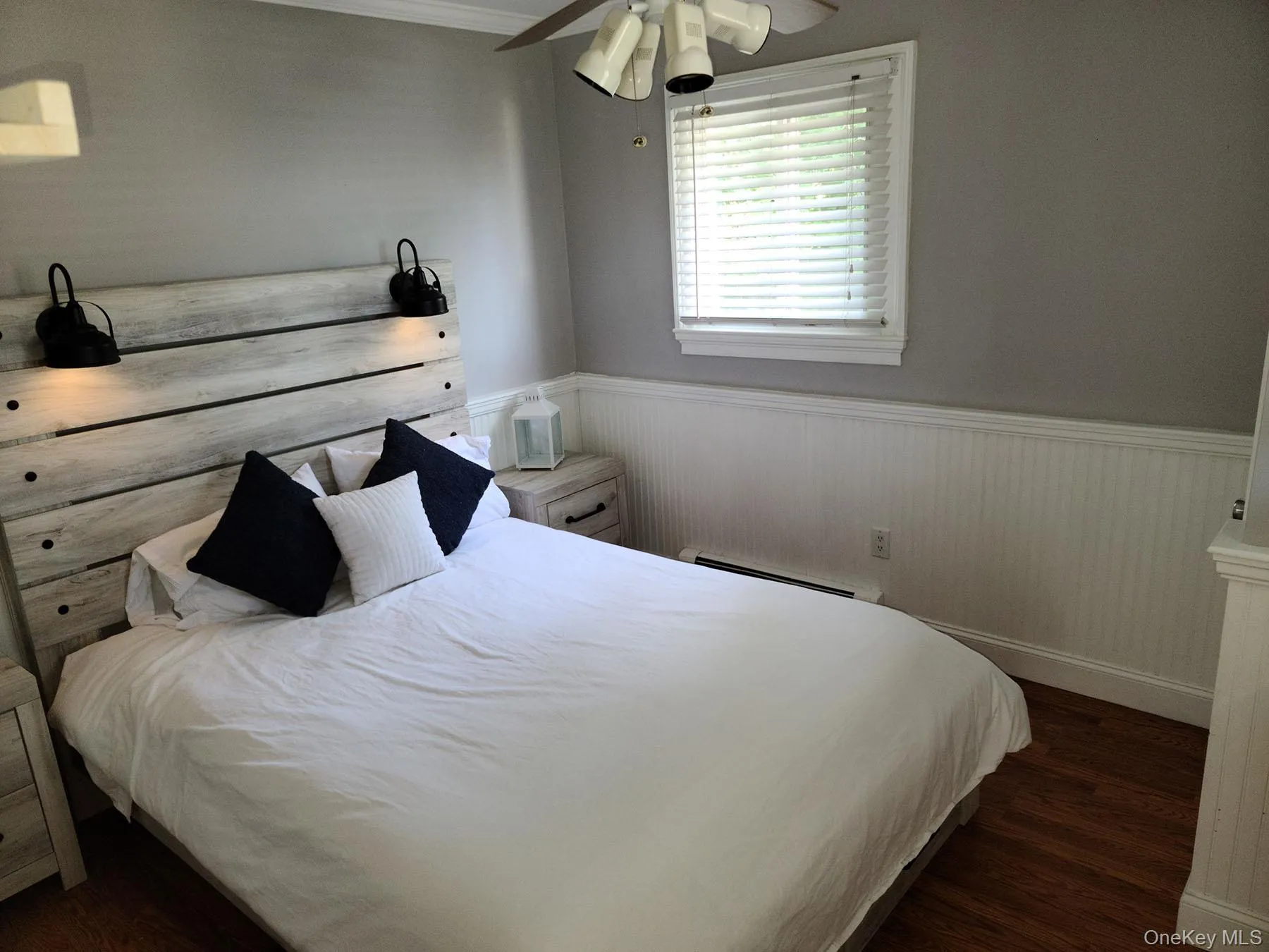 Bedroom featuring dark wood-style flooring, wainscoting, baseboard heating, and ceiling fan Bedroom featuring dark wood-style flooring, wainscoting, baseboard heating, and ceiling fan