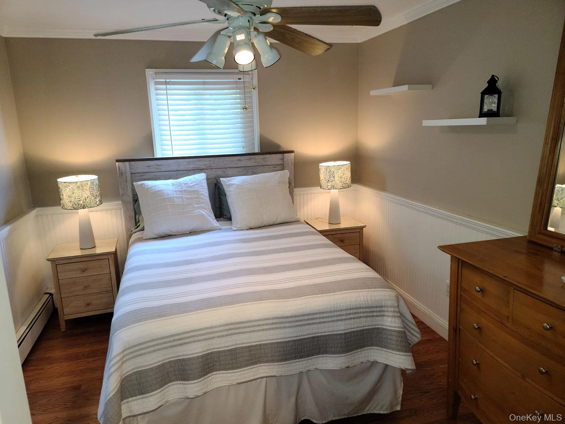 Bedroom featuring a wainscoted wall, baseboard heating, crown molding, dark wood-style flooring, and ceiling fan Bedroom featuring a wainscoted wall, baseboard heating, crown molding, dark wood-style flooring, and ceiling fan