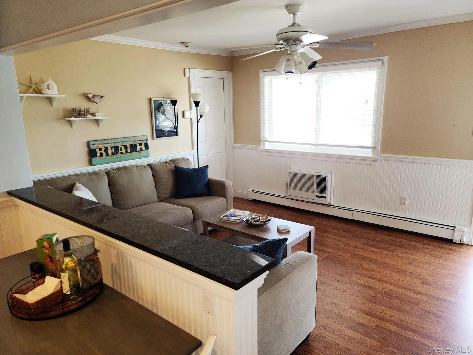 Living area featuring a wainscoted wall, a baseboard heating unit, dark wood-type flooring, crown molding, and ceiling fan Living area featuring a wainscoted wall, a baseboard heating unit, dark wood-type flooring, crown molding, and ceiling fan