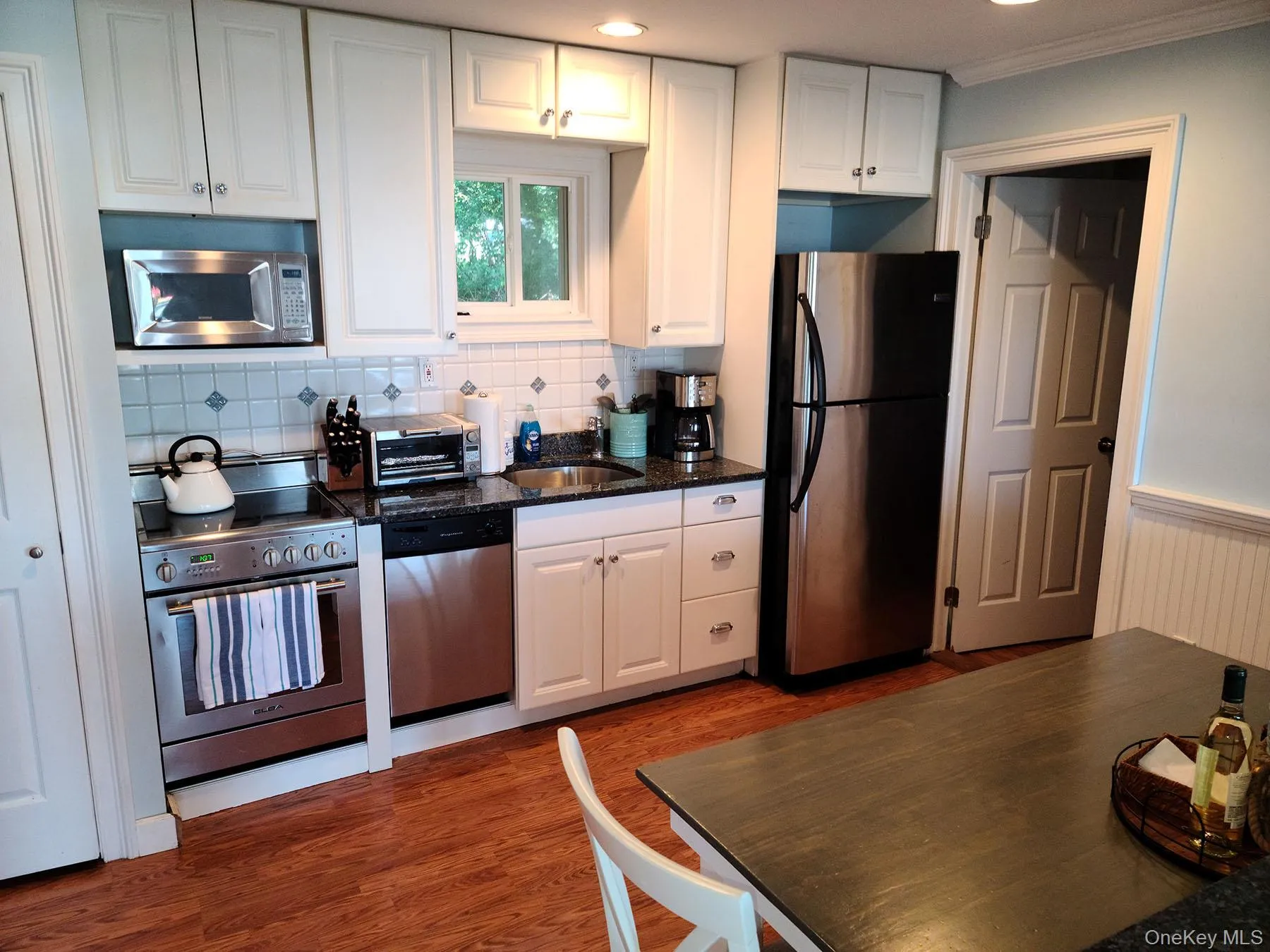 Kitchen with white cabinets, dark stone countertops, appliances with stainless steel finishes, backsplash, and dark wood-style floors Kitchen with white cabinets, dark stone countertops, appliances with stainless steel finishes, backsplash, and dark wood-style floors