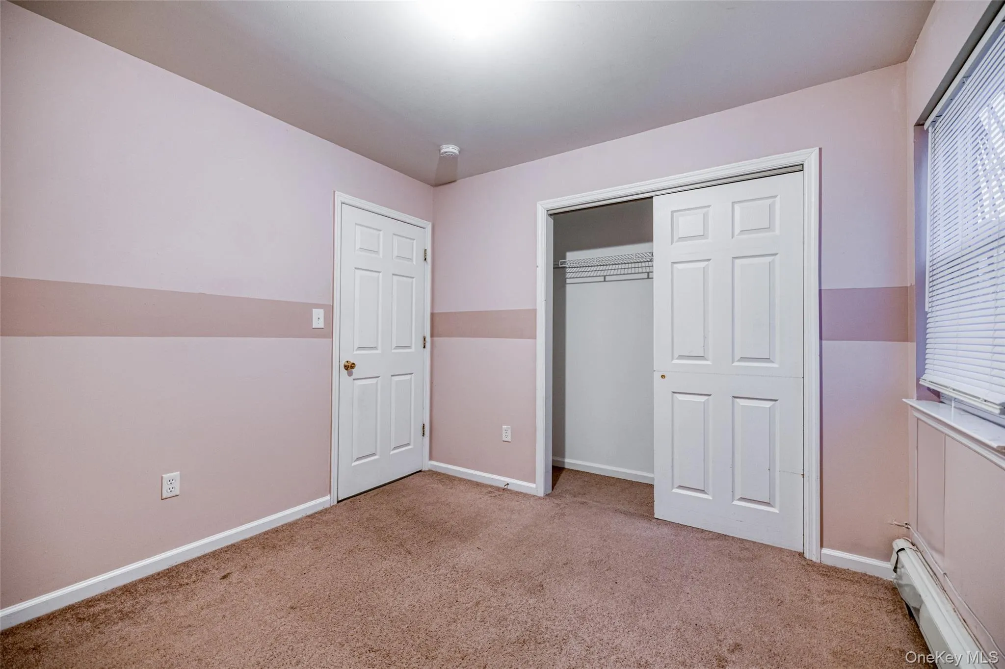Unfurnished bedroom featuring baseboard heating, light colored carpet, and a closet Unfurnished bedroom featuring baseboard heating, light colored carpet, and a closet