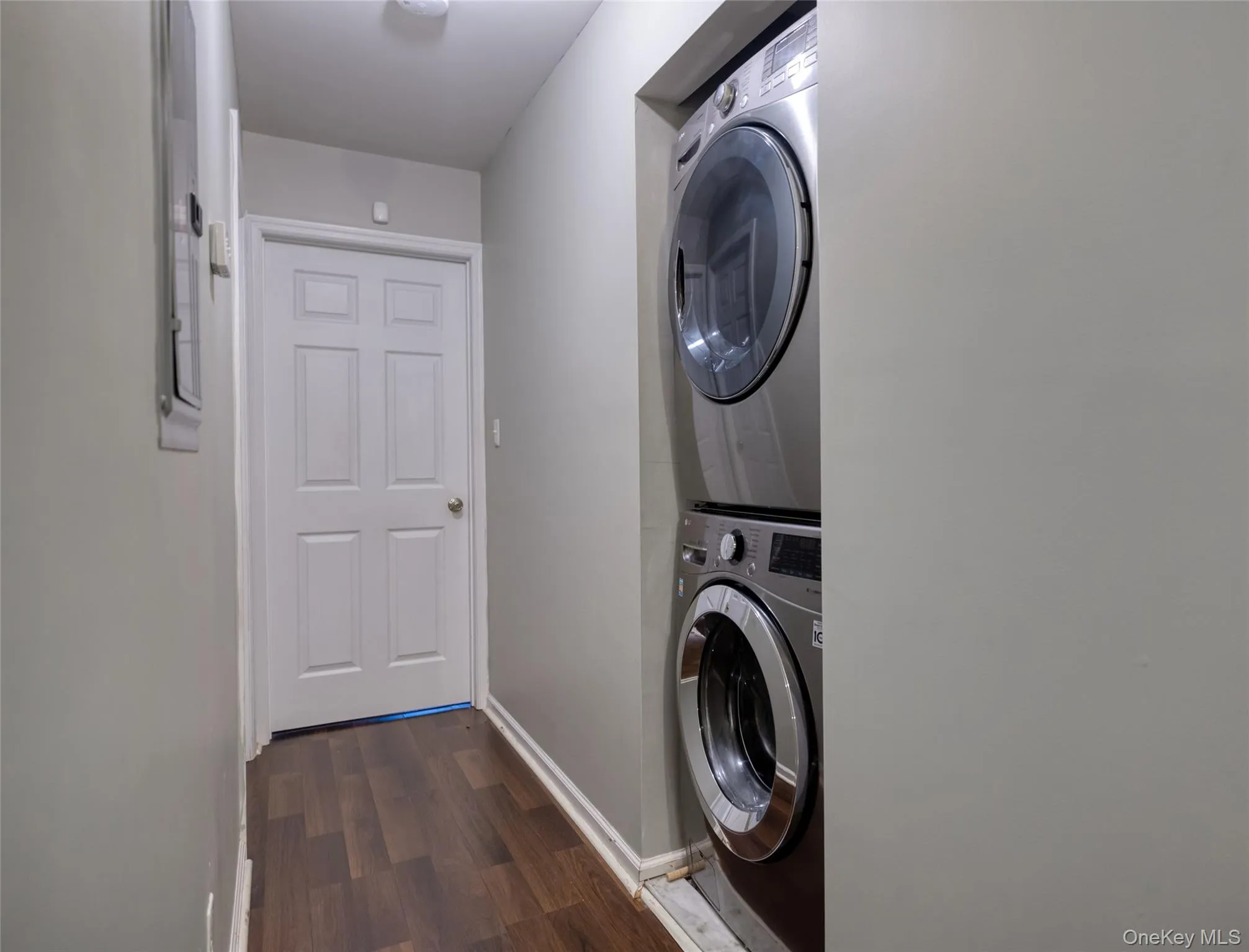 Washroom with dark wood-style floors and stacked washing machine and dryer Washroom with dark wood-style floors and stacked washing machine and dryer