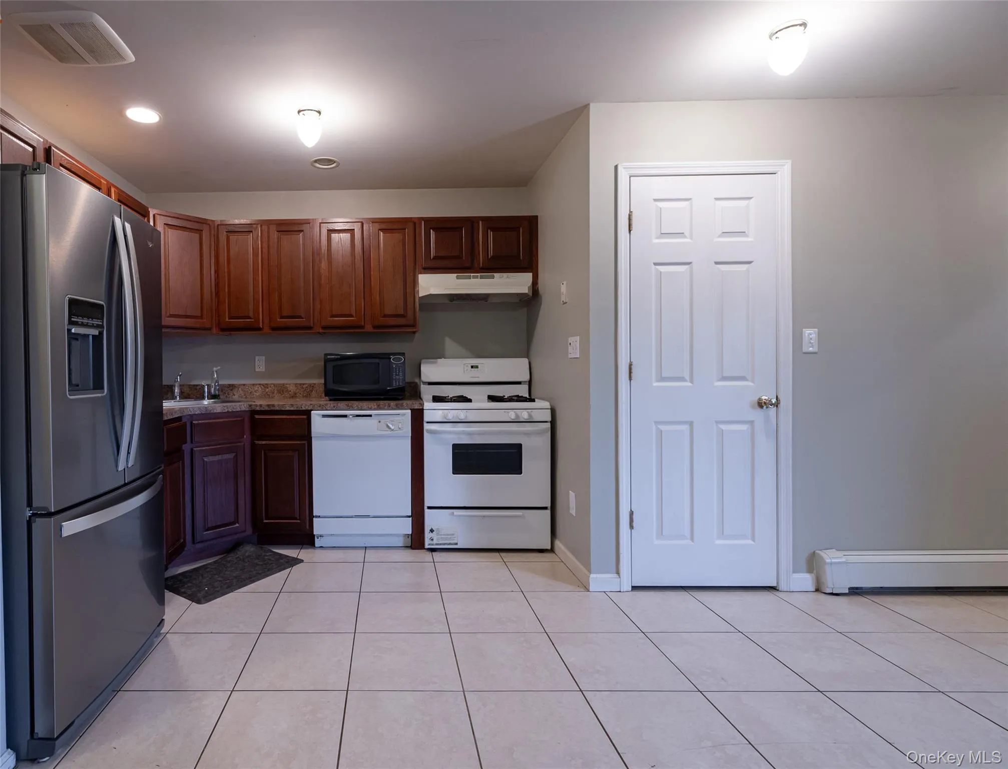 Kitchen with white appliances, light tile patterned flooring, under cabinet range hood, a baseboard radiator, and recessed lighting Kitchen with white appliances, light tile patterned flooring, under cabinet range hood, a baseboard radiator, and recessed lighting