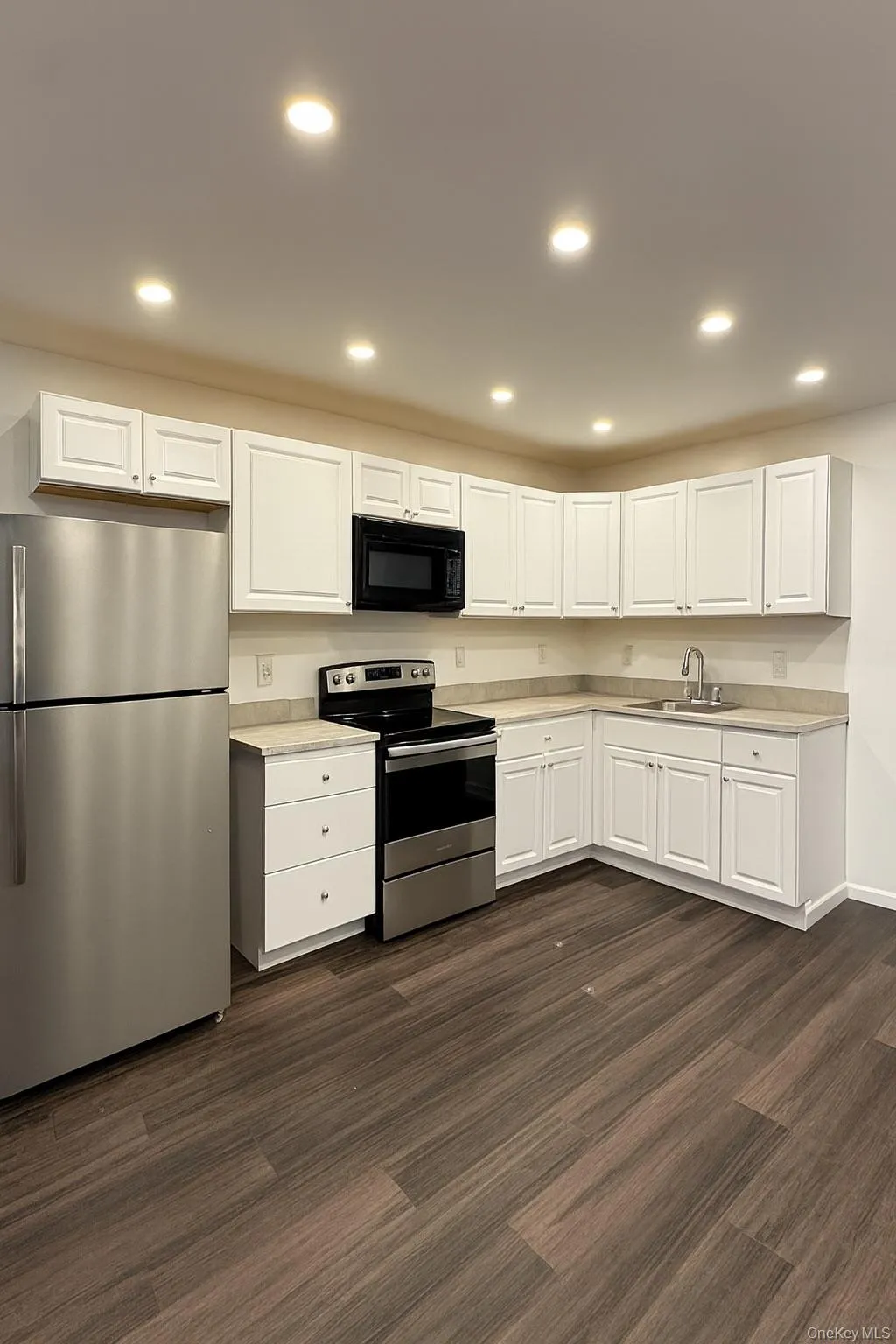 Kitchen with appliances with stainless steel finishes, white cabinetry, recessed lighting, dark wood-style flooring, and light countertops Kitchen with appliances with stainless steel finishes, white cabinetry, recessed lighting, dark wood-style flooring, and light countertops
