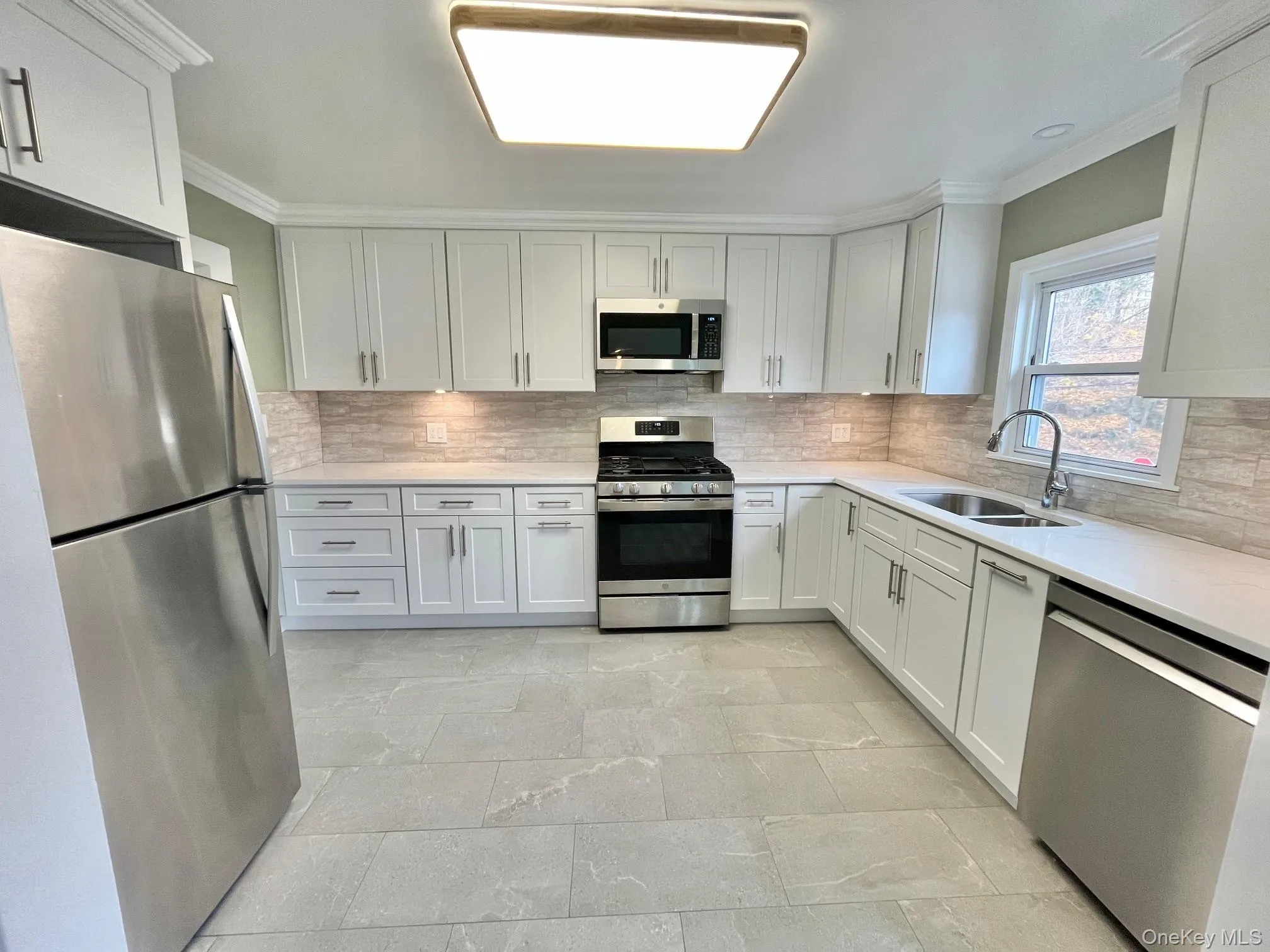 Kitchen with appliances with stainless steel finishes, white cabinetry, ornamental molding, light stone countertops, and tasteful backsplash Kitchen with appliances with stainless steel finishes, white cabinetry, ornamental molding, light stone countertops, and tasteful backsplash