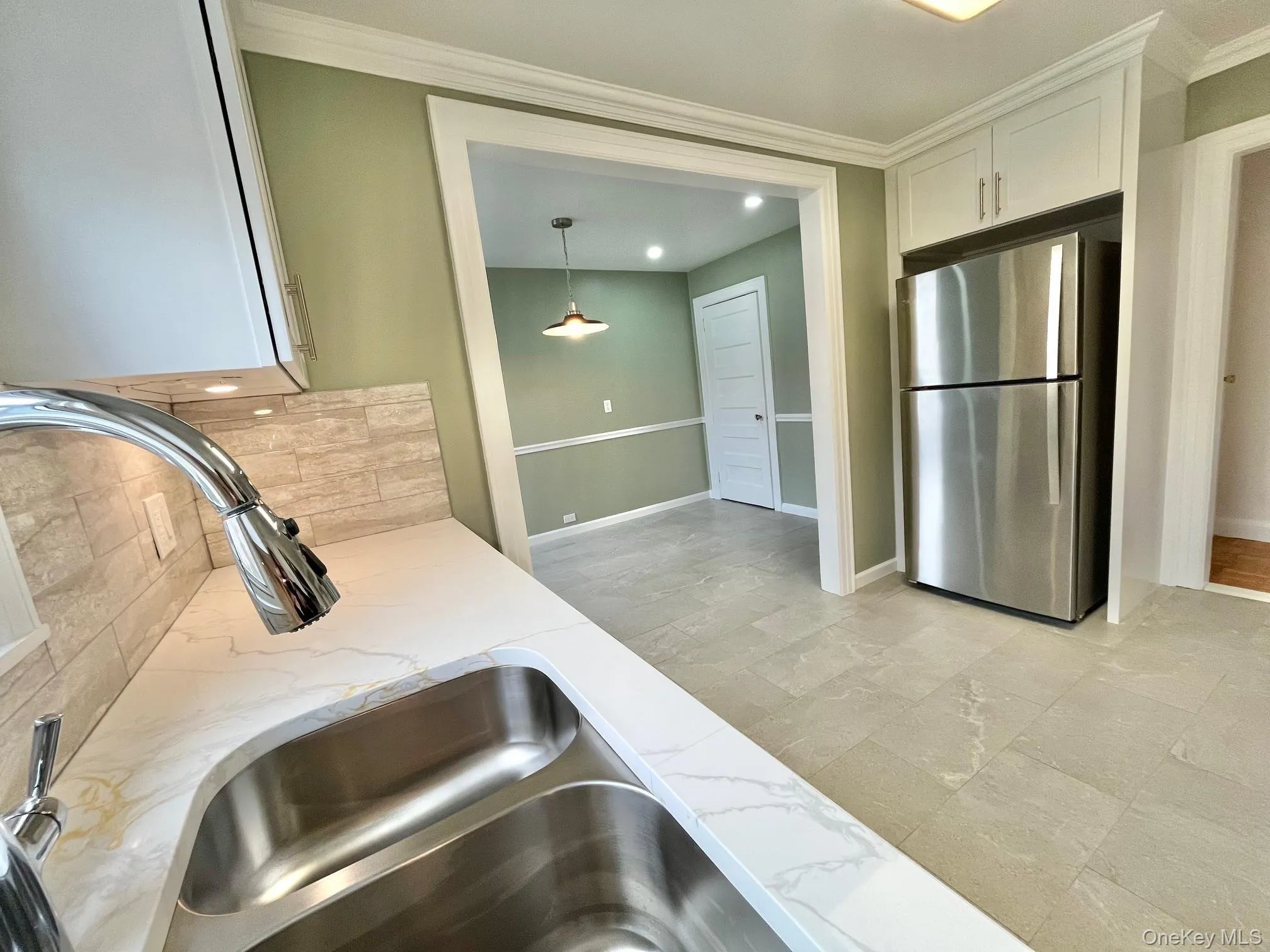 Kitchen featuring freestanding refrigerator, crown molding, pendant lighting, light stone countertops, and white cabinetry Kitchen featuring freestanding refrigerator, crown molding, pendant lighting, light stone countertops, and white cabinetry