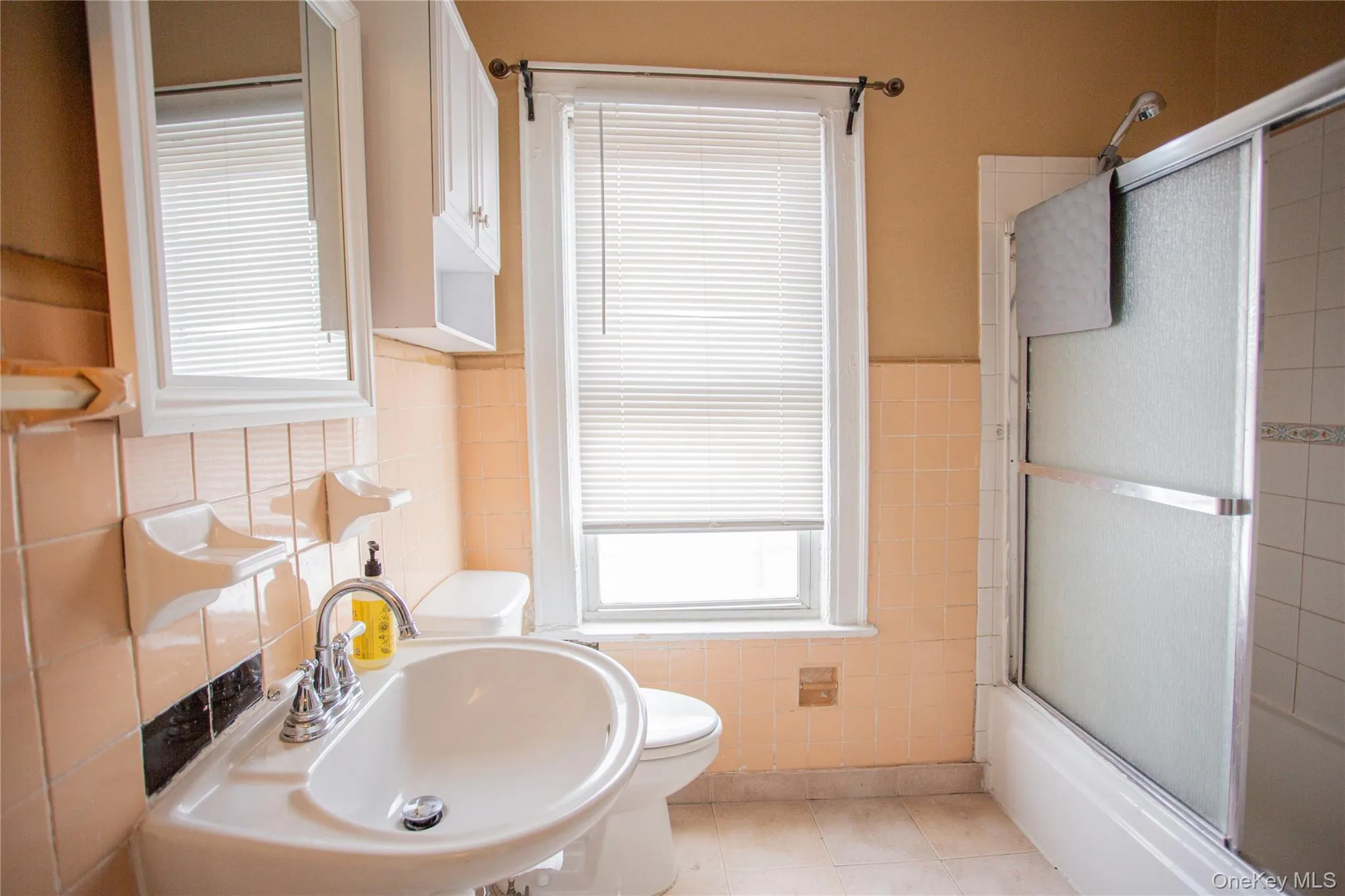 Bathroom with tile walls, bath / shower combo with glass door, healthy amount of natural light, a wainscoted wall, and light tile patterned flooring Bathroom with tile walls, bath / shower combo with glass door, healthy amount of natural light, a wainscoted wall, and light tile patterned flooring