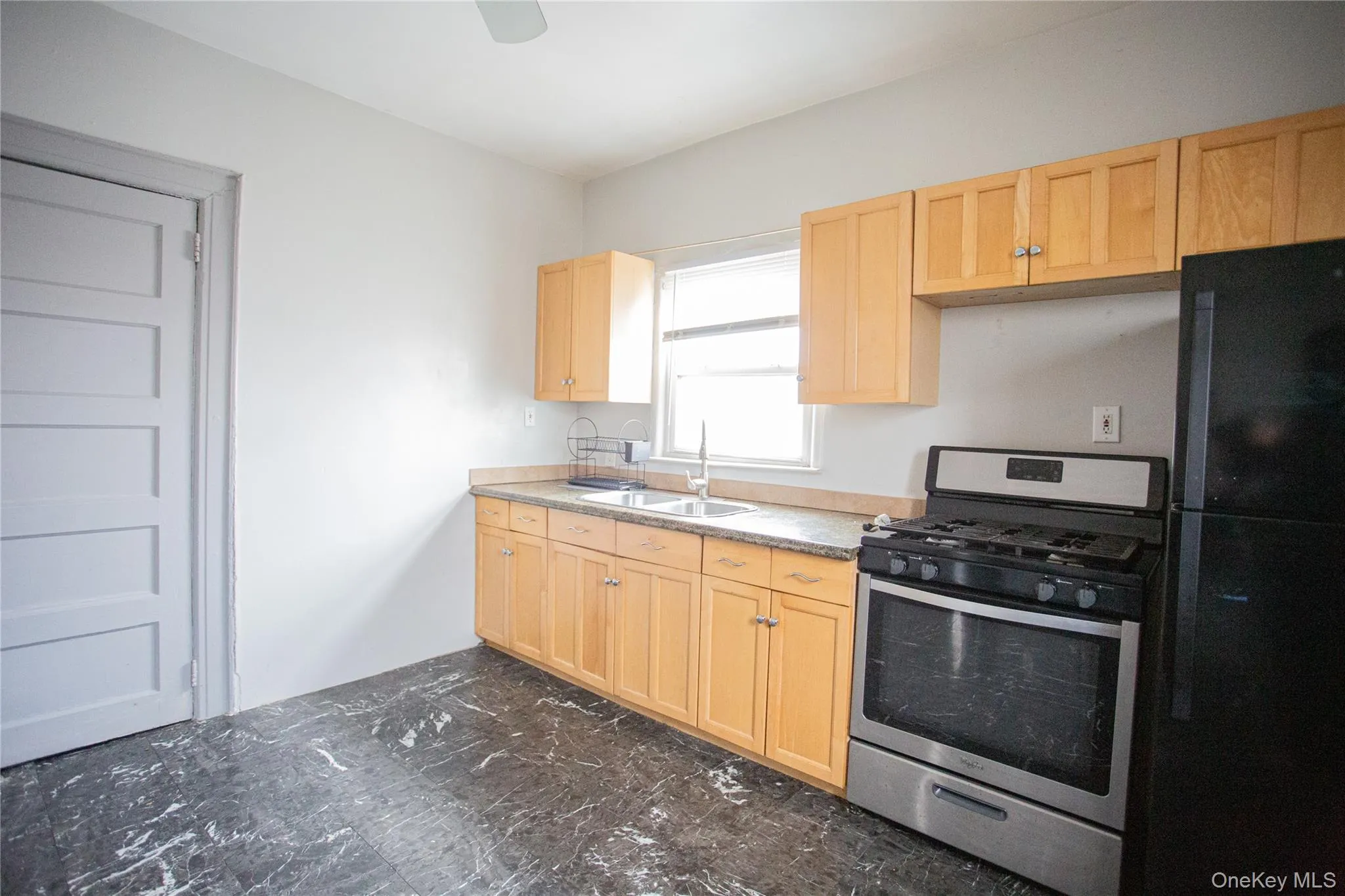 Kitchen featuring light brown cabinetry, gas range, freestanding refrigerator, light countertops, and dark marble finish flooring Kitchen featuring light brown cabinetry, gas range, freestanding refrigerator, light countertops, and dark marble finish flooring