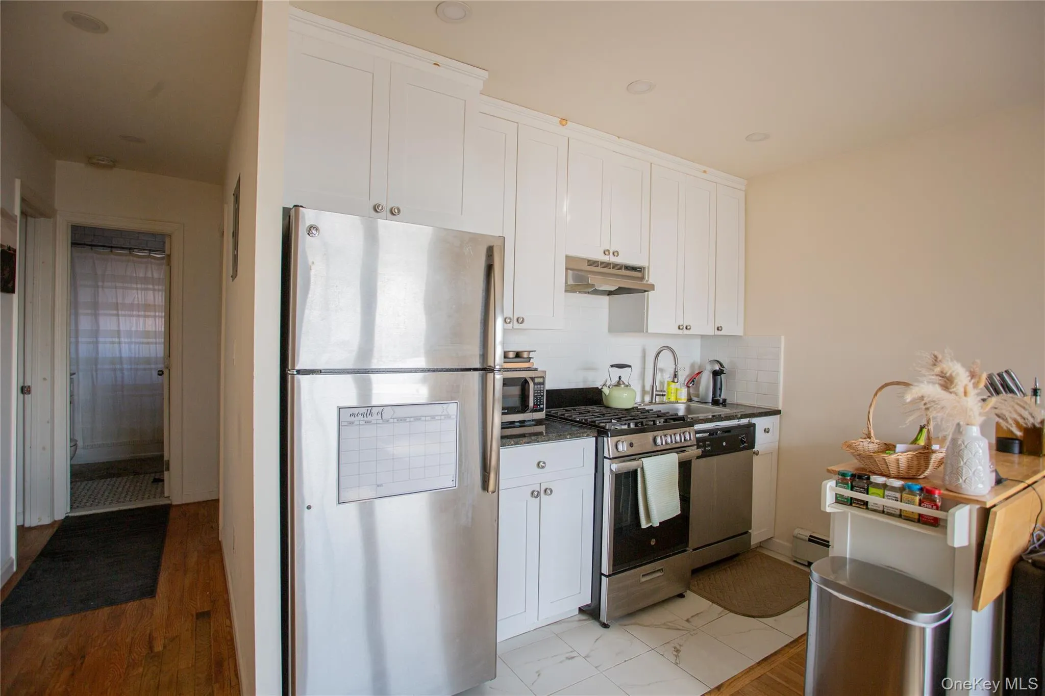 Kitchen featuring stainless steel appliances, white cabinets, under cabinet range hood, backsplash, and dark stone counters Kitchen featuring stainless steel appliances, white cabinets, under cabinet range hood, backsplash, and dark stone counters