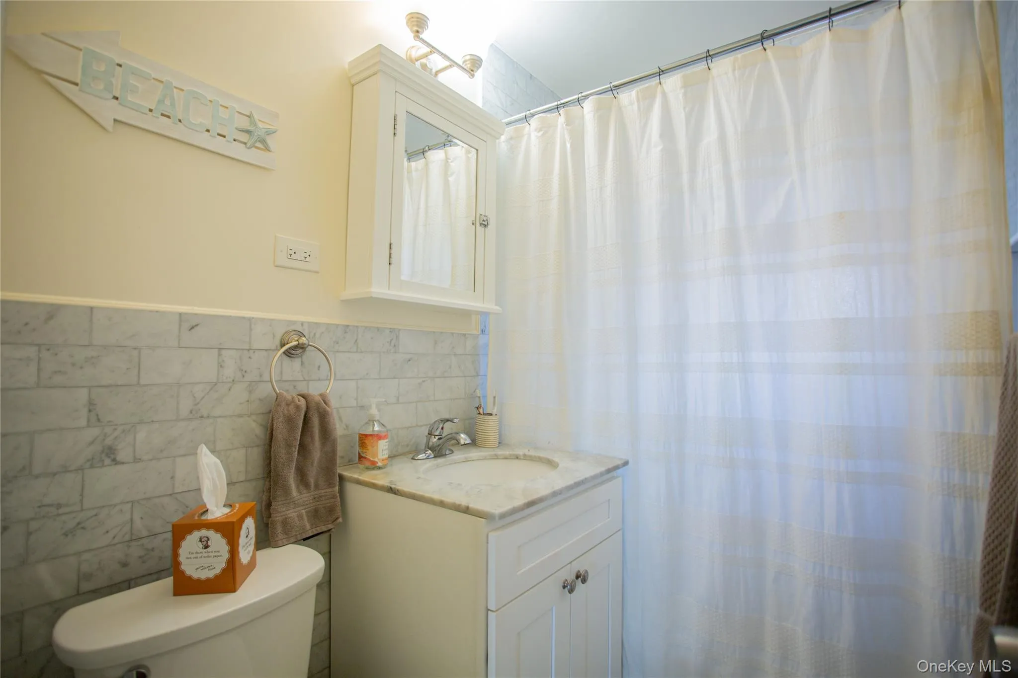 Full bath featuring tile walls, a shower with curtain, vanity, and wainscoting Full bath featuring tile walls, a shower with curtain, vanity, and wainscoting
