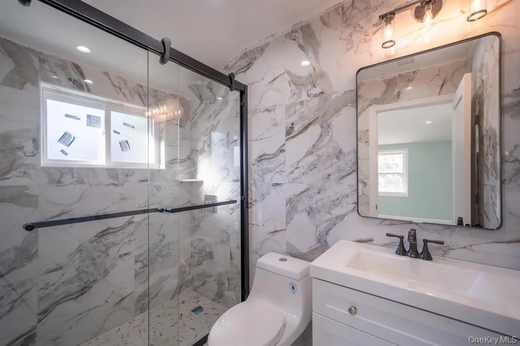 Bathroom with healthy amount of natural light, vanity, a marble finish shower, and stone wall Bathroom with healthy amount of natural light, vanity, a marble finish shower, and stone wall