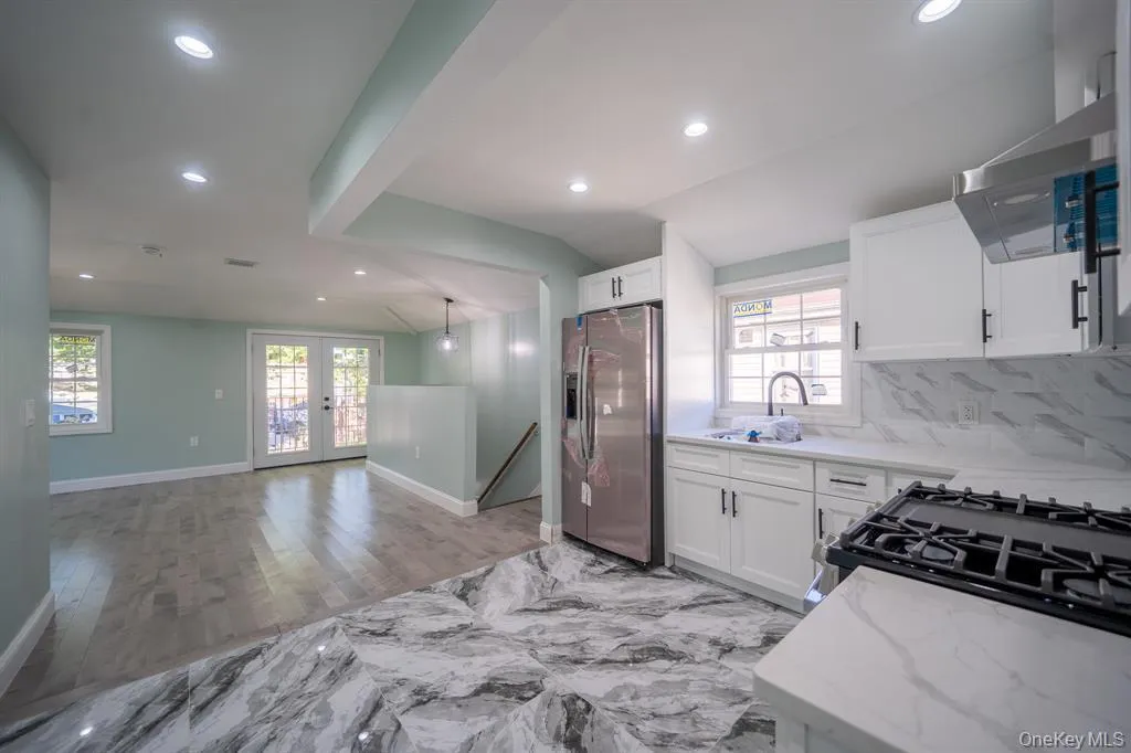 Kitchen featuring lofted ceiling, stainless steel fridge with ice dispenser, white cabinets, recessed lighting, and french doors Kitchen featuring lofted ceiling, stainless steel fridge with ice dispenser, white cabinets, recessed lighting, and french doors
