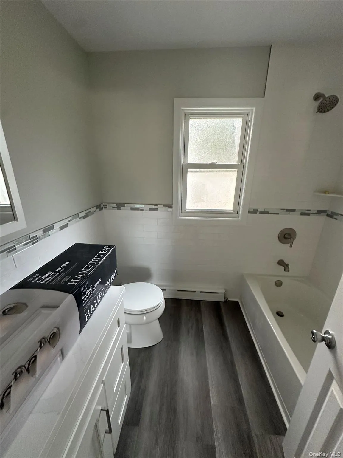 Full bath with vanity, tile walls, dark wood-style flooring, shower combination, and a baseboard radiator Full bath with vanity, tile walls, dark wood-style flooring, shower combination, and a baseboard radiator