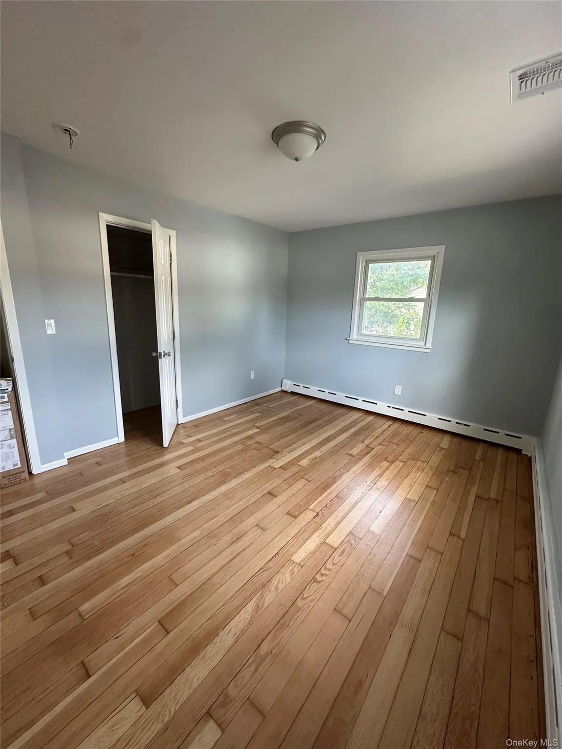 Unfurnished bedroom featuring a spacious closet, a baseboard heating unit, and light wood-style floors Unfurnished bedroom featuring a spacious closet, a baseboard heating unit, and light wood-style floors