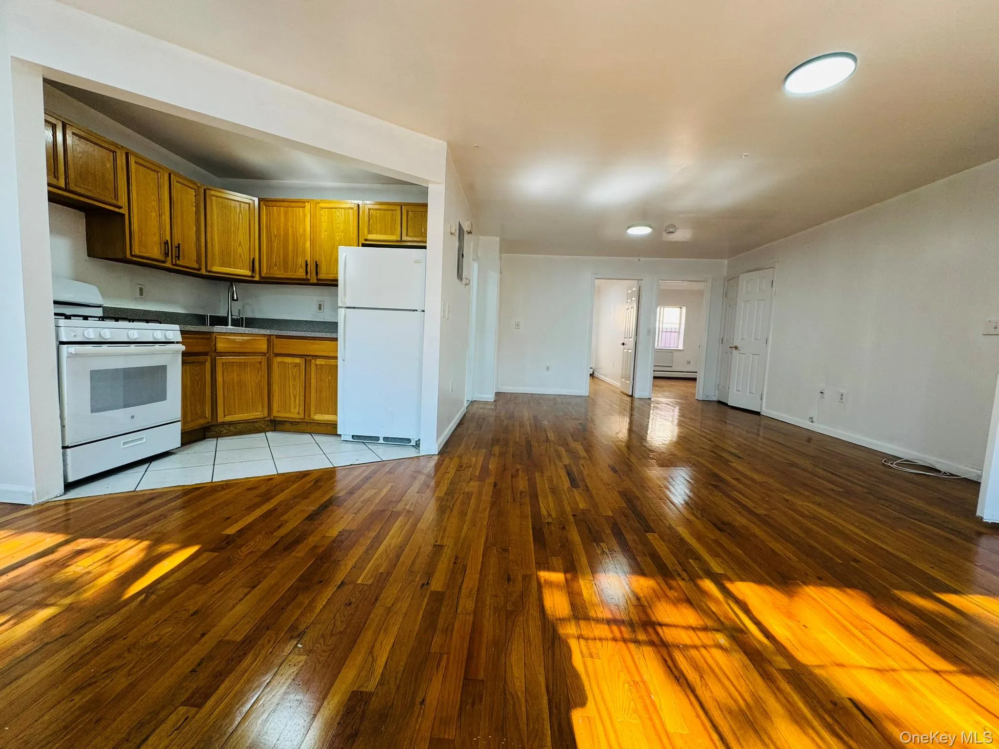 Kitchen featuring white appliances, brown cabinets, light wood-style floors, open floor plan, and dark countertops Kitchen featuring white appliances, brown cabinets, light wood-style floors, open floor plan, and dark countertops